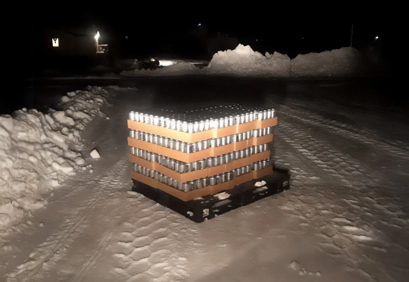 Stack of Kuuk cans on a pallet in a snowy outdoor setting at night.