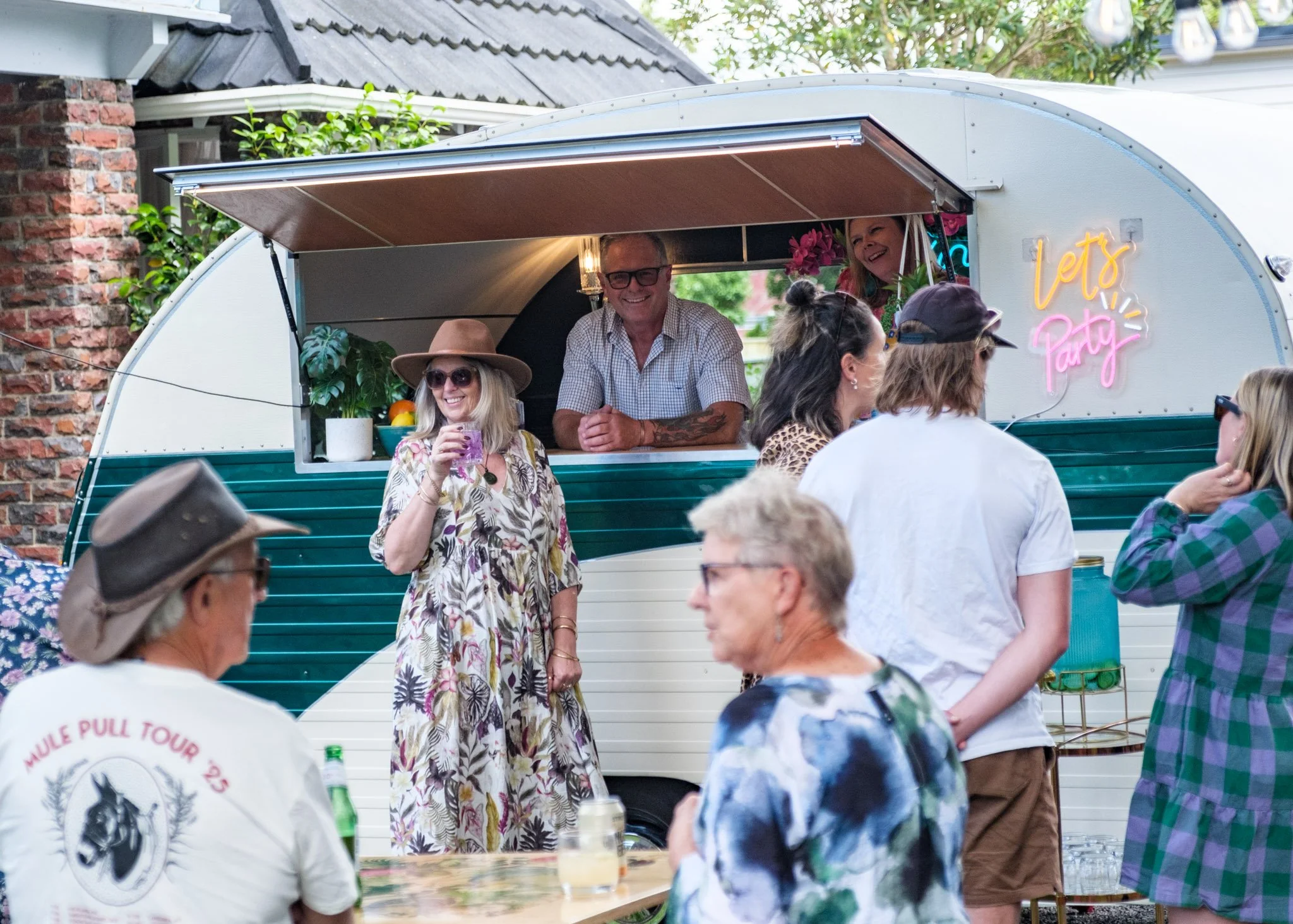 People socializing at a backyard party near 'Winnie-Bar-Go' the mobile caravan bar