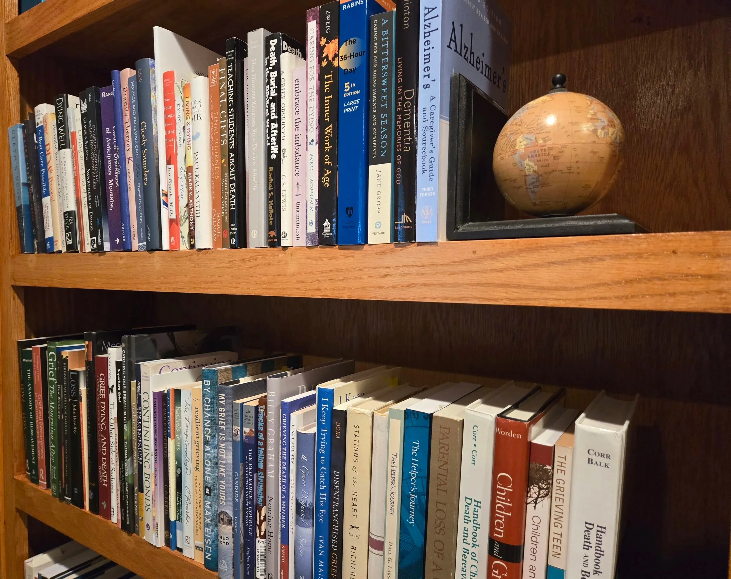 Bookshelf with two shelves filled with books, and a decorative globe on the top shelf.