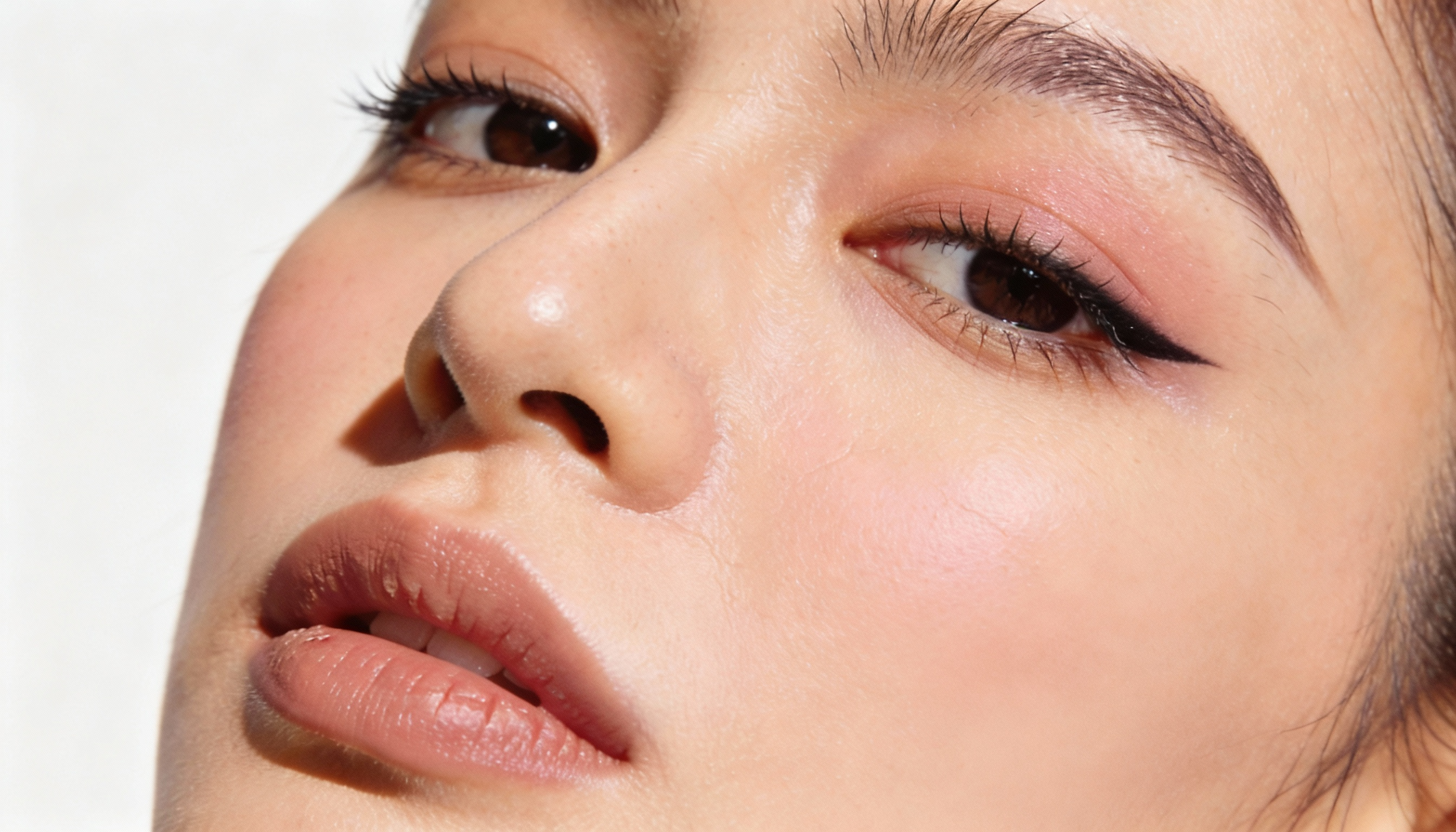 Close-up of a woman’s face showing her nose, lips, and eyes with makeup, featuring well-groomed eyebrows, eyeliner, and eyeshadow.