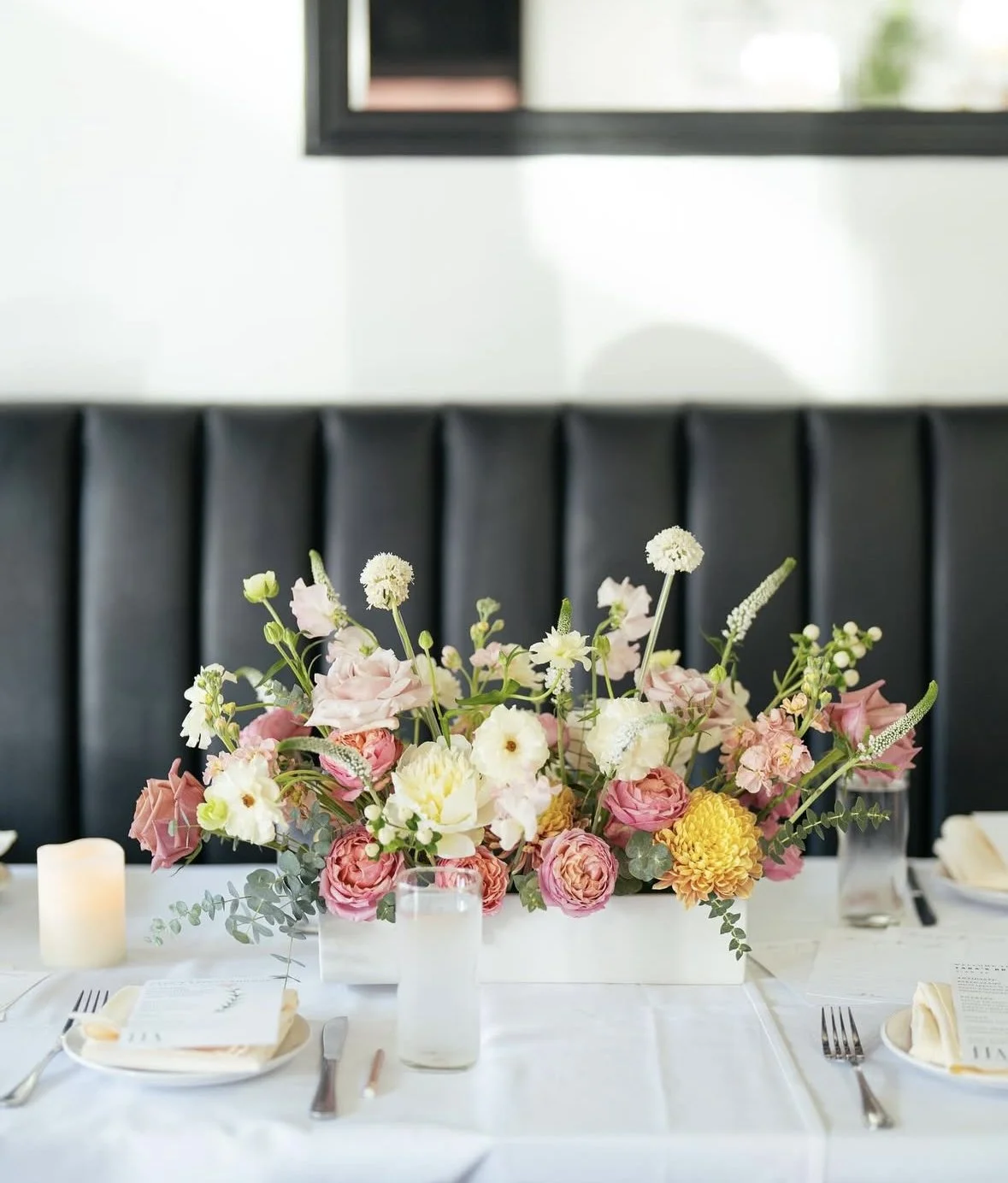 Colorful spring centerpiece with coral and yellow flowers on white linen table.