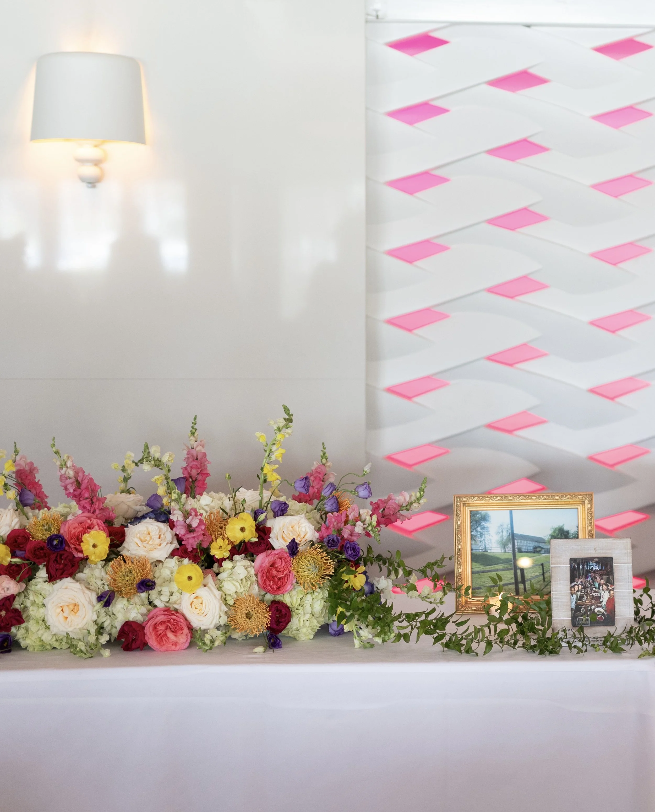 Long head table with vibrant pink and multicolor floral arrangements