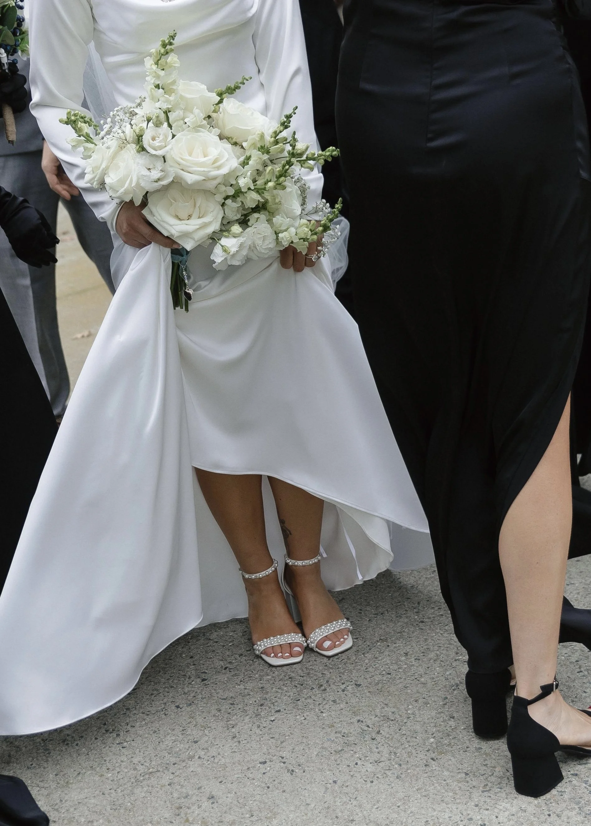 Modern asymmetrical wedding dress detail with flowing fabric holding all white bouquet