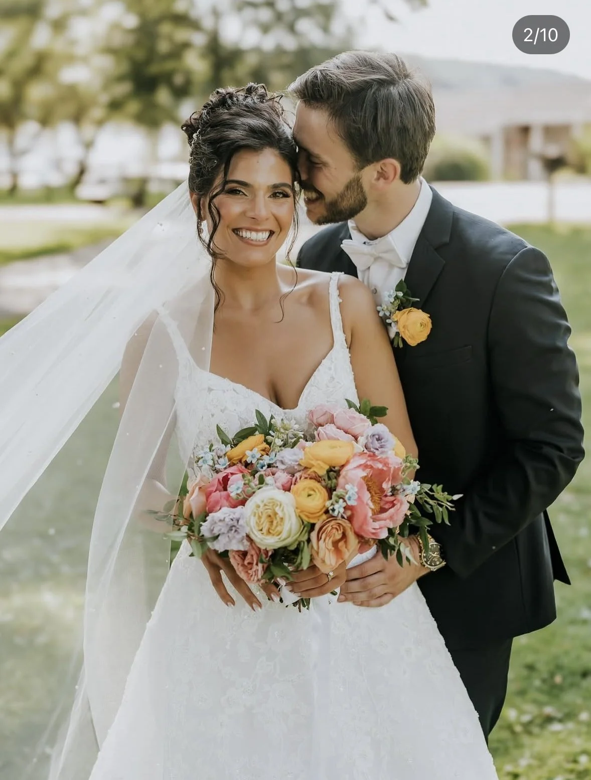 Bride holding vibrant coral and pink bouquet with groom at outdoor Long Island wedding.