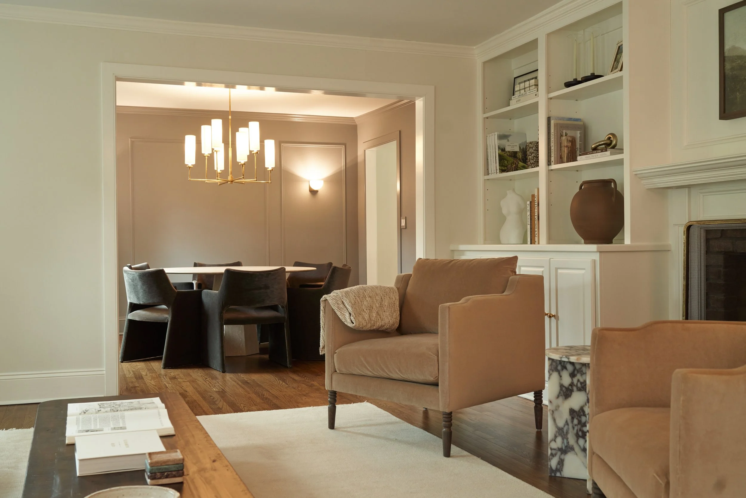 Transitional living and dining space with built-in storage, tan chairs, and marble side table