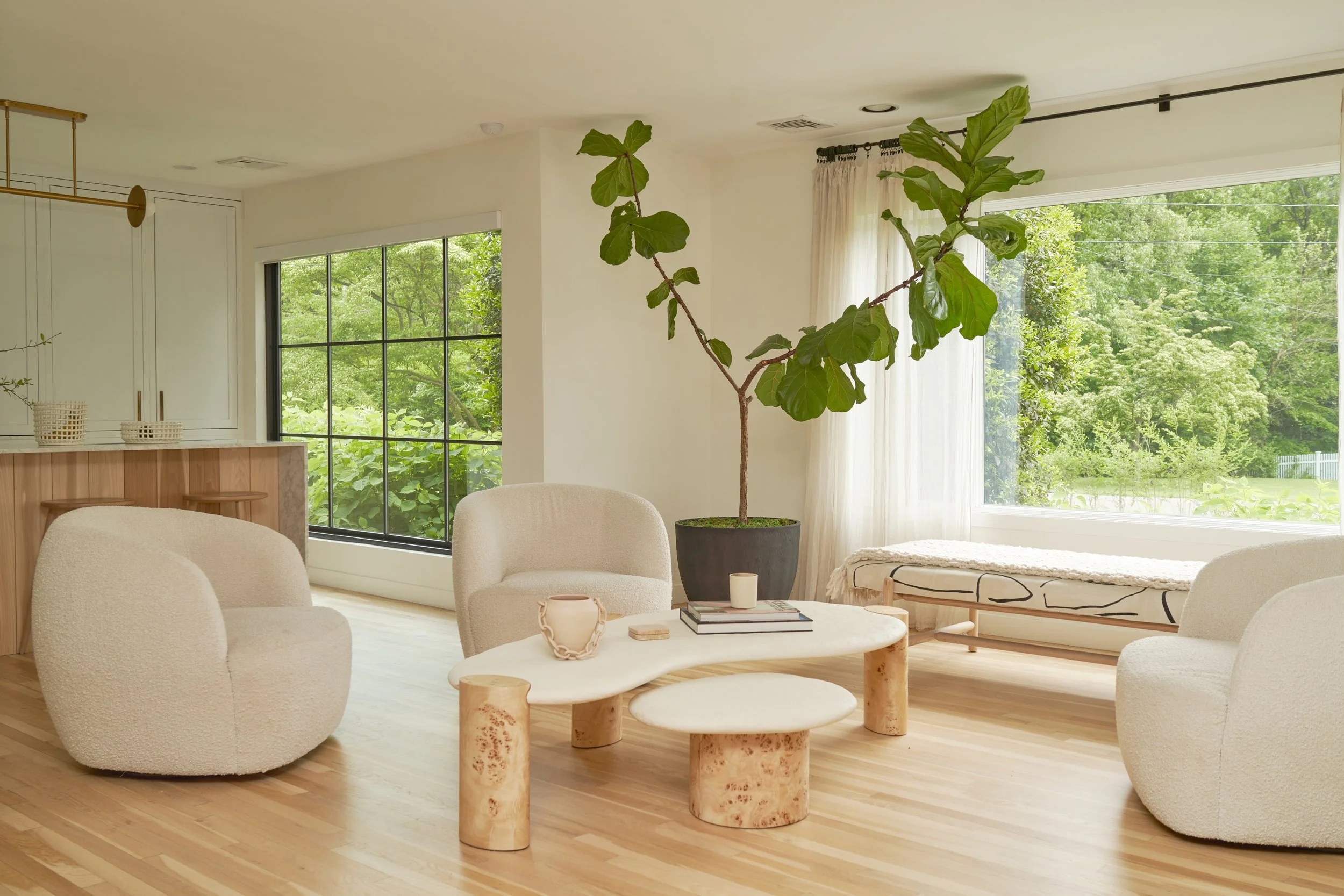 Serene modern living room with natural wood tree stump tables, fiddle leaf fig, and black grid windows