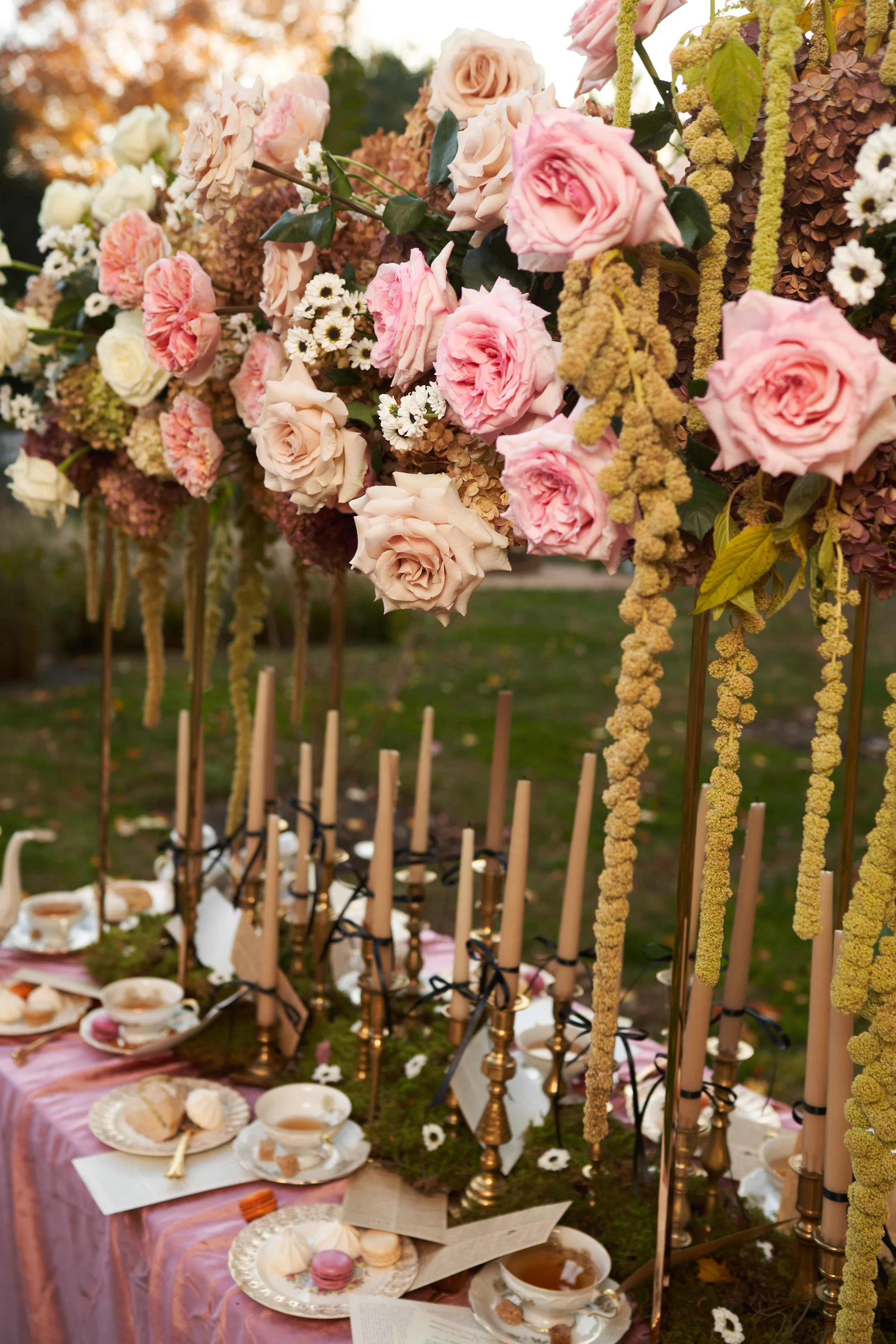 Tall pink rose and greenery centerpieces with taper candles on outdoor wedding table.