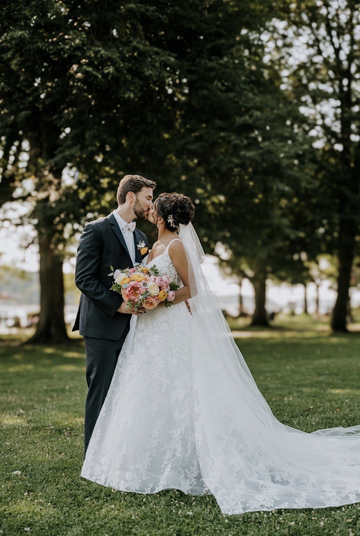 Couple kissing under trees with colorful coral and pink wedding bouquet