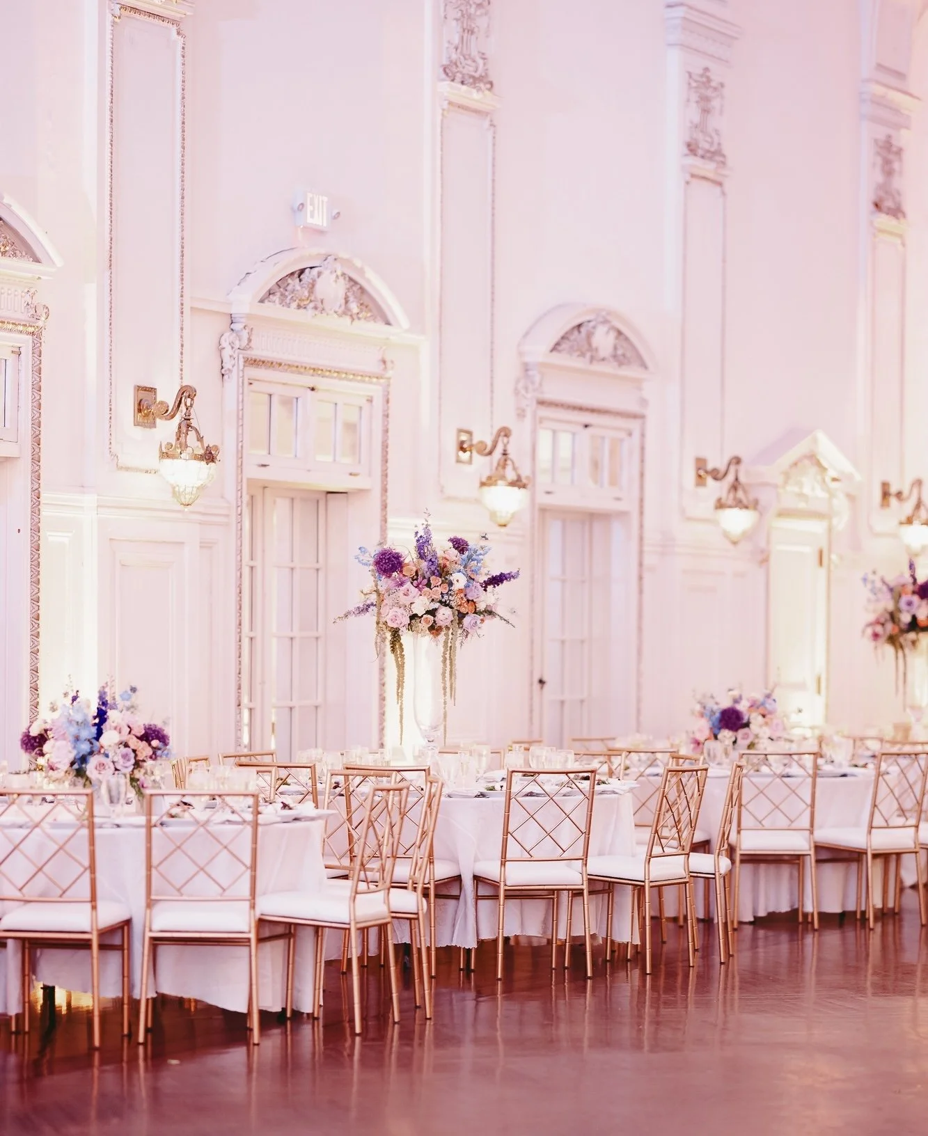 Elegant wedding reception with rose gold chiavari chairs, blush linens, and tall purple and white floral centerpieces on Long Island