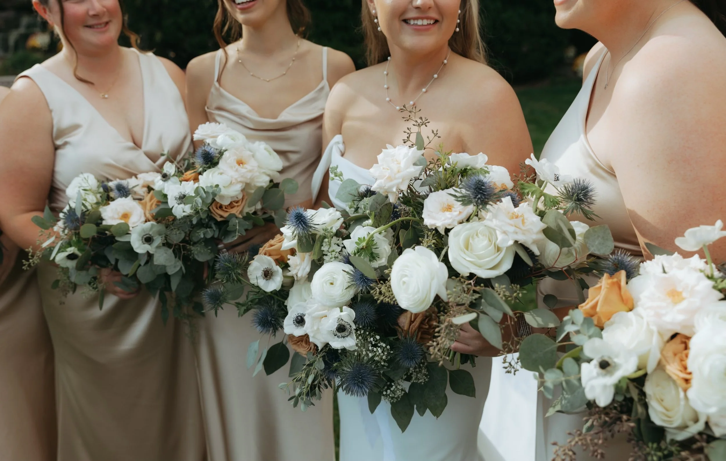 Four bridesmaids in neutral gowns holding white, blush and green wedding bouquets