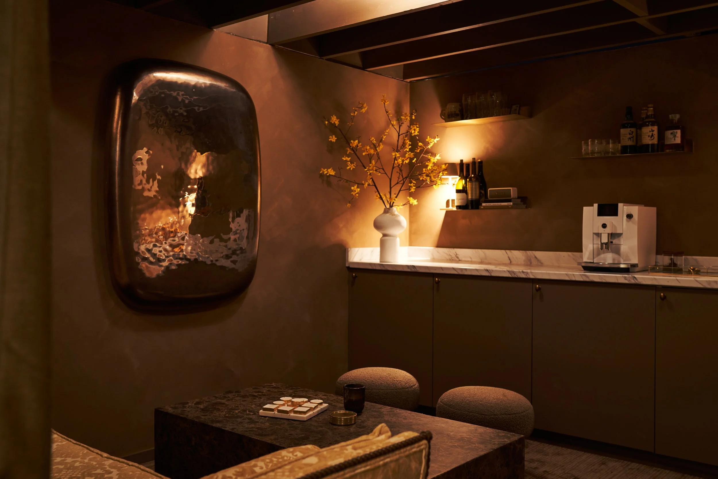 Modern moody interior design featuring dark marble table with tan leather ottomans and warm lighting by Nicole Link Designs