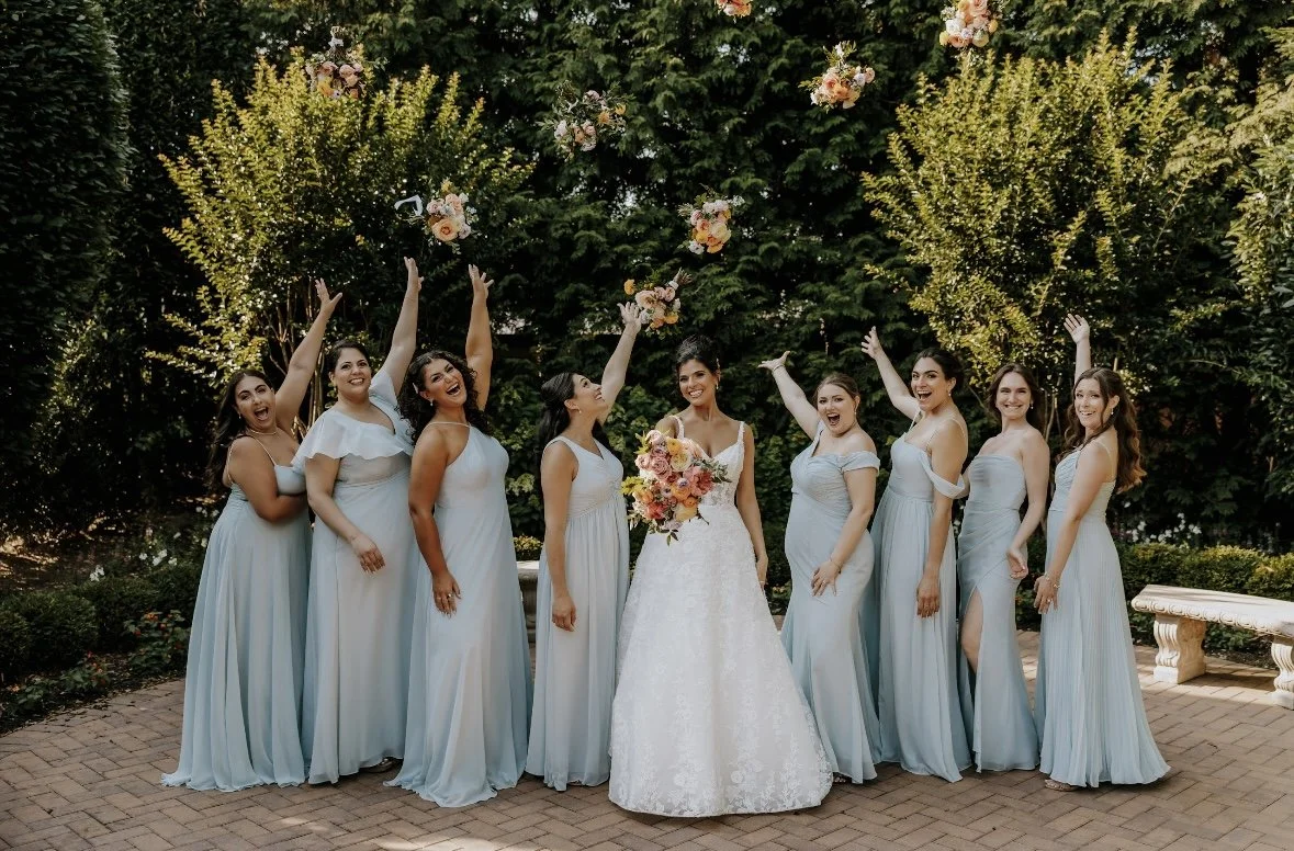 Bridesmaids in sage green dresses raising bouquets in celebration