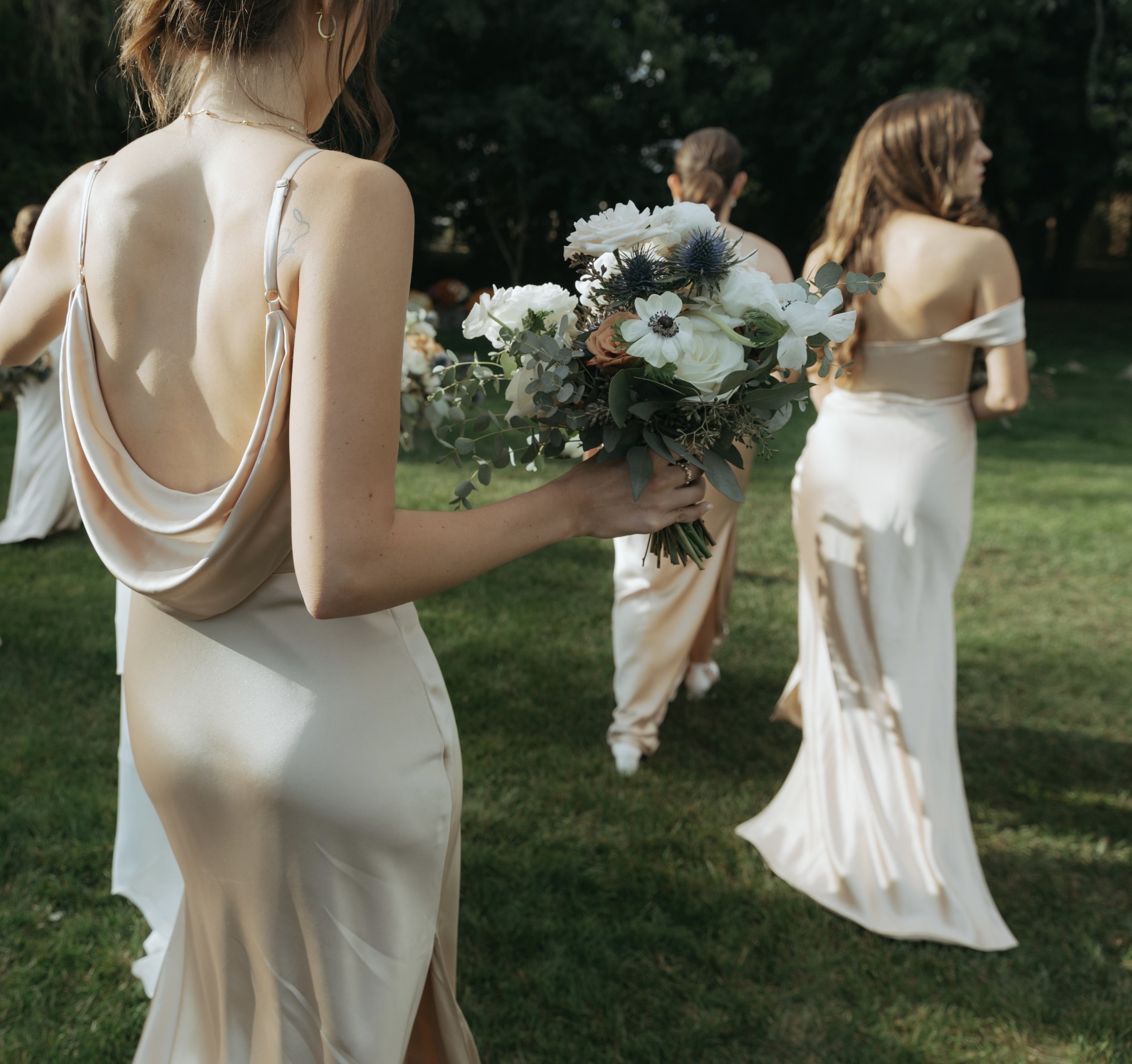 Bridesmaids in silk slip dresses with pearl back details and white bouquets.