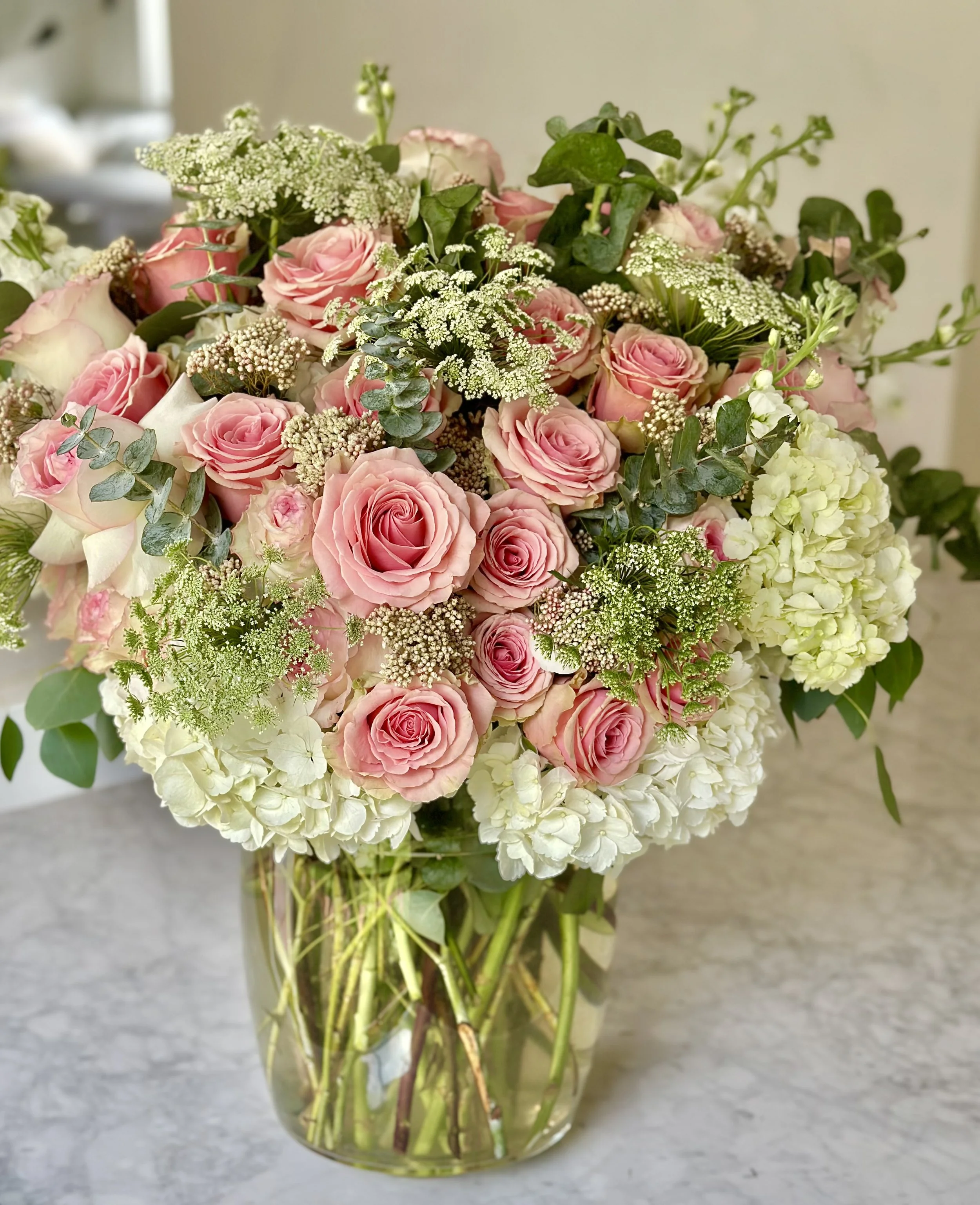 Garden-style arrangement with pink roses and green hydrangeas in clear vase.