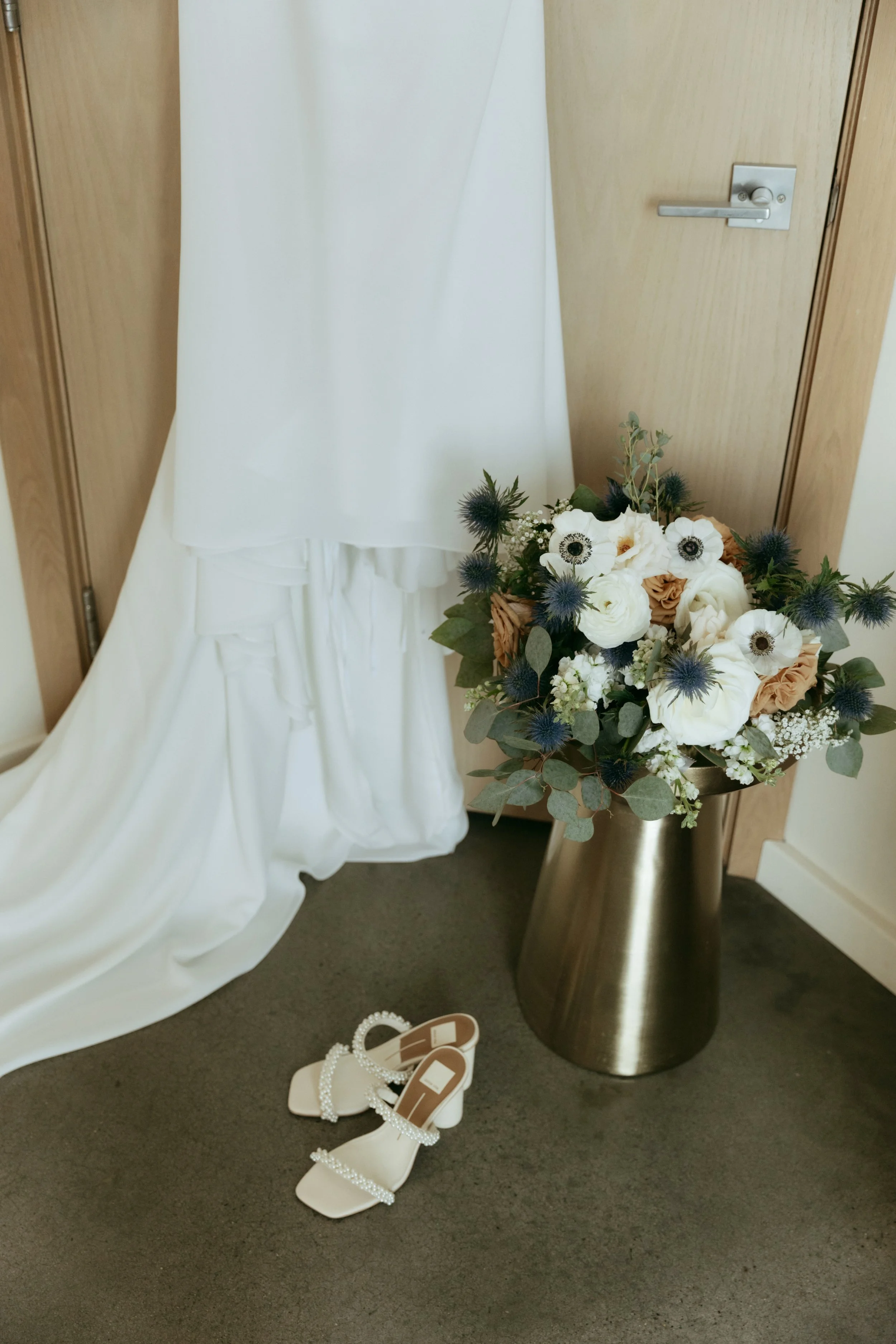 White and green wedding bouquet in gold vase on neutral backdrop.