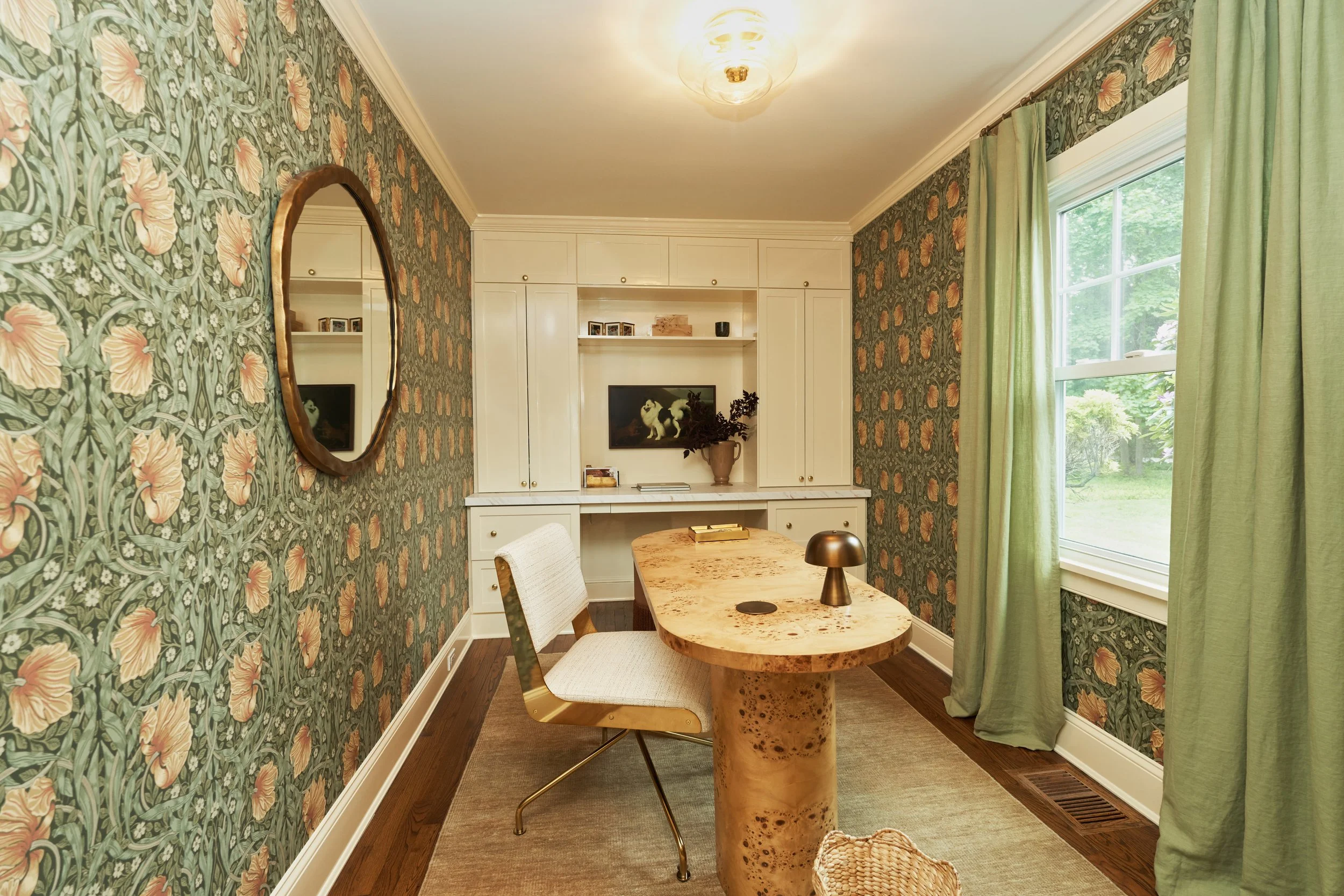 Cozy sitting area with statement floral wallpaper, round brass mirror, and burl wood furniture