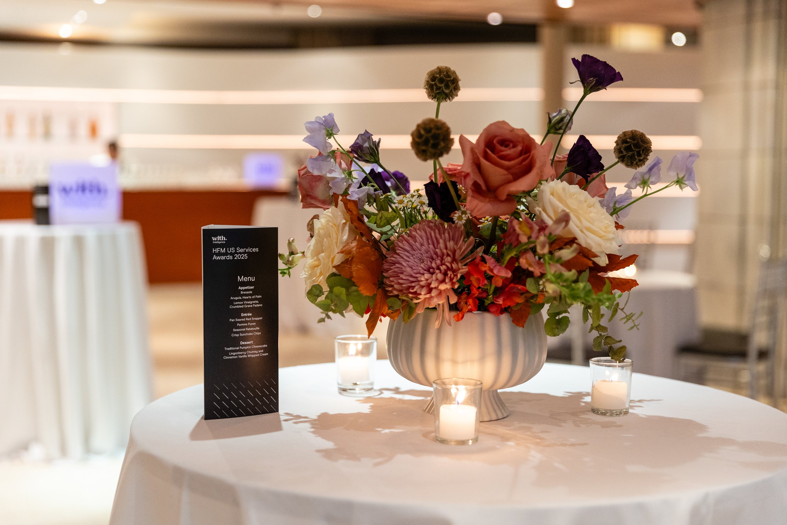 Jewel-toned fall centerpiece with burgundy and coral flowers in pedestal vase