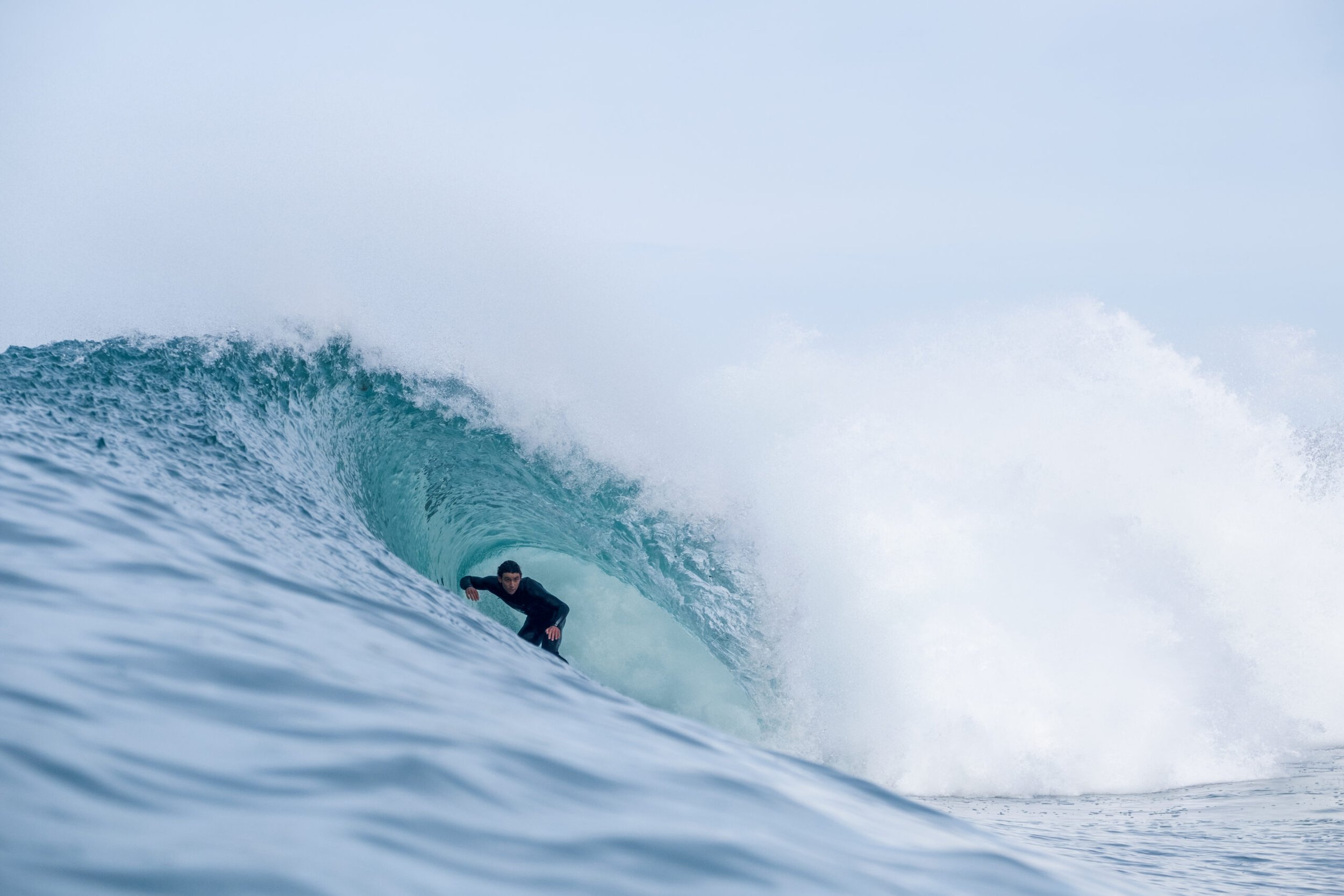 A surfer riding inside the barrel of a large ocean wave with light blue water and white spray in the background.
