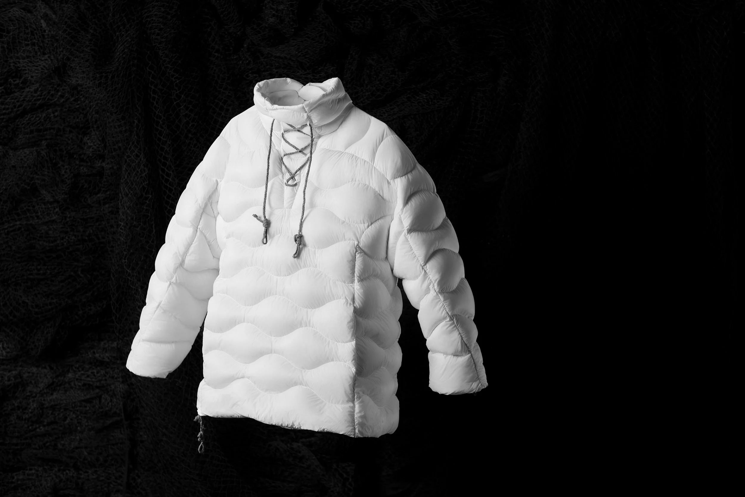 A white puffer jacket with a high collar and drawstrings against a dark background.