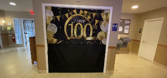 Decorative display celebrating 100th anniversary with gold and black balloons, and a sign that says 'Happy 100th'.