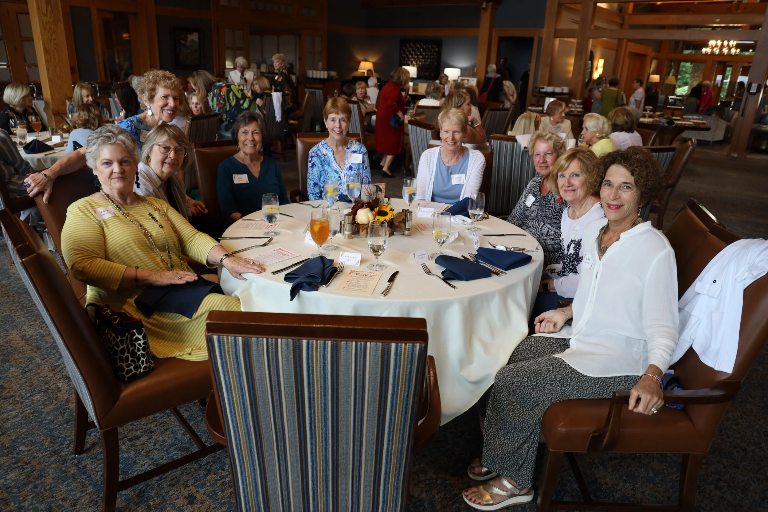 A group of women sitting around a round table at an event or banquet in a warmly decorated restaurant or banquet hall.