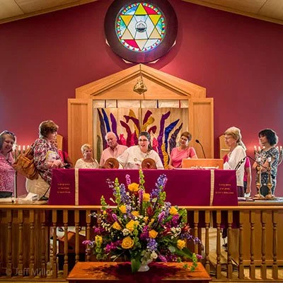 People gathered around an altar with a purple cloth, flowers, and a cross inside a church with stained glass above.