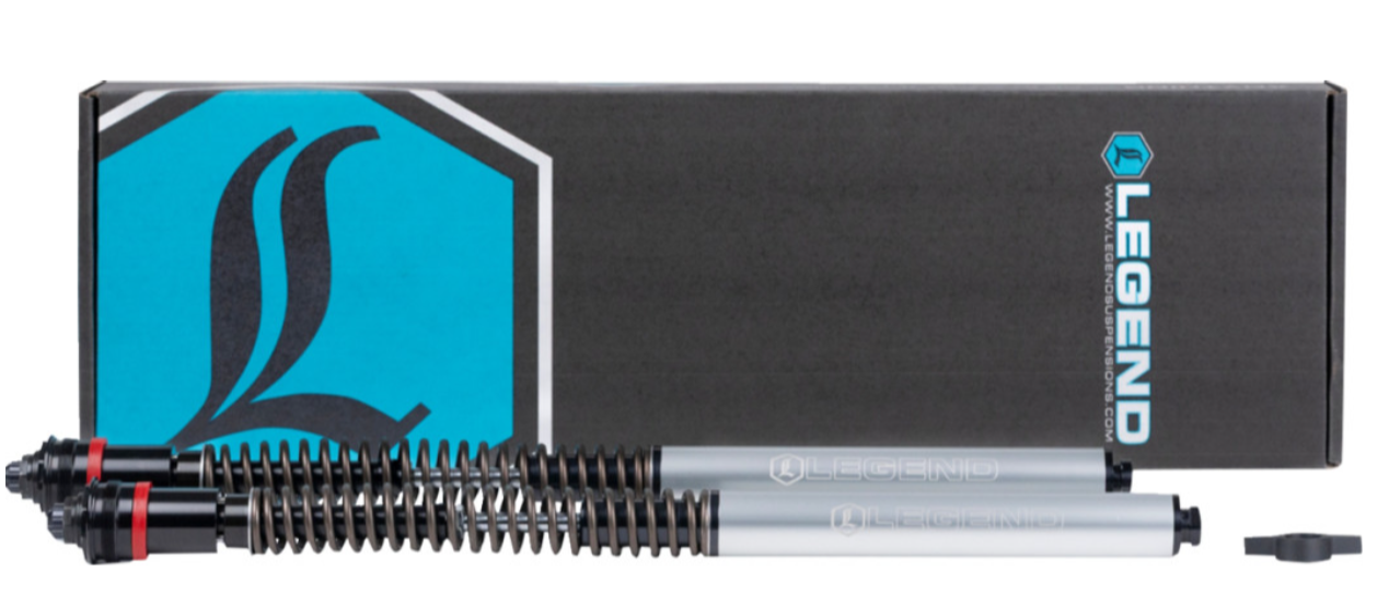 Two suspension forks with coil springs placed in front of a Legend box packaging, which is black with a blue logo and text.