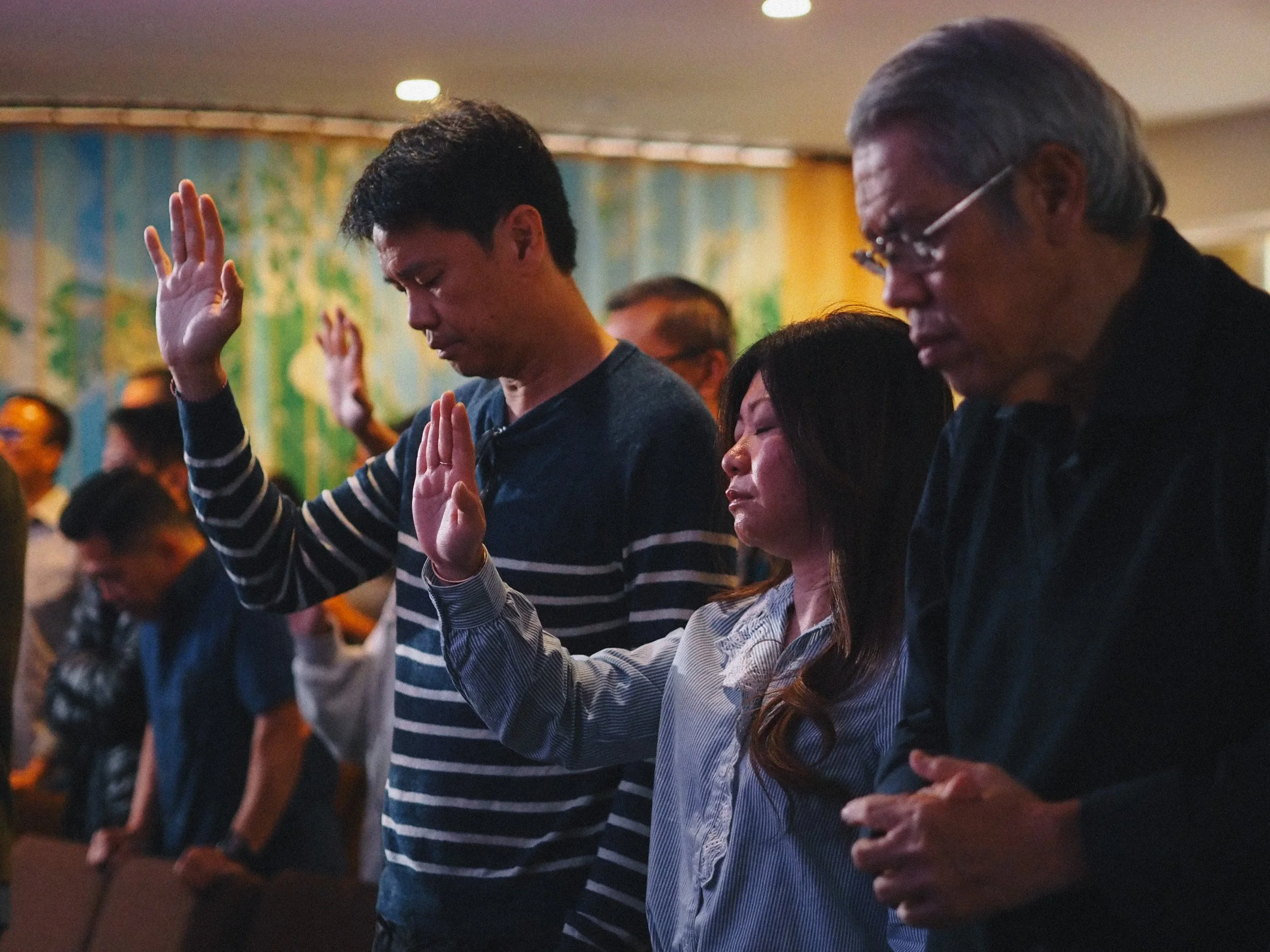 People in prayer with eyes closed, hands raised, and heads bowed during Sunday Service.