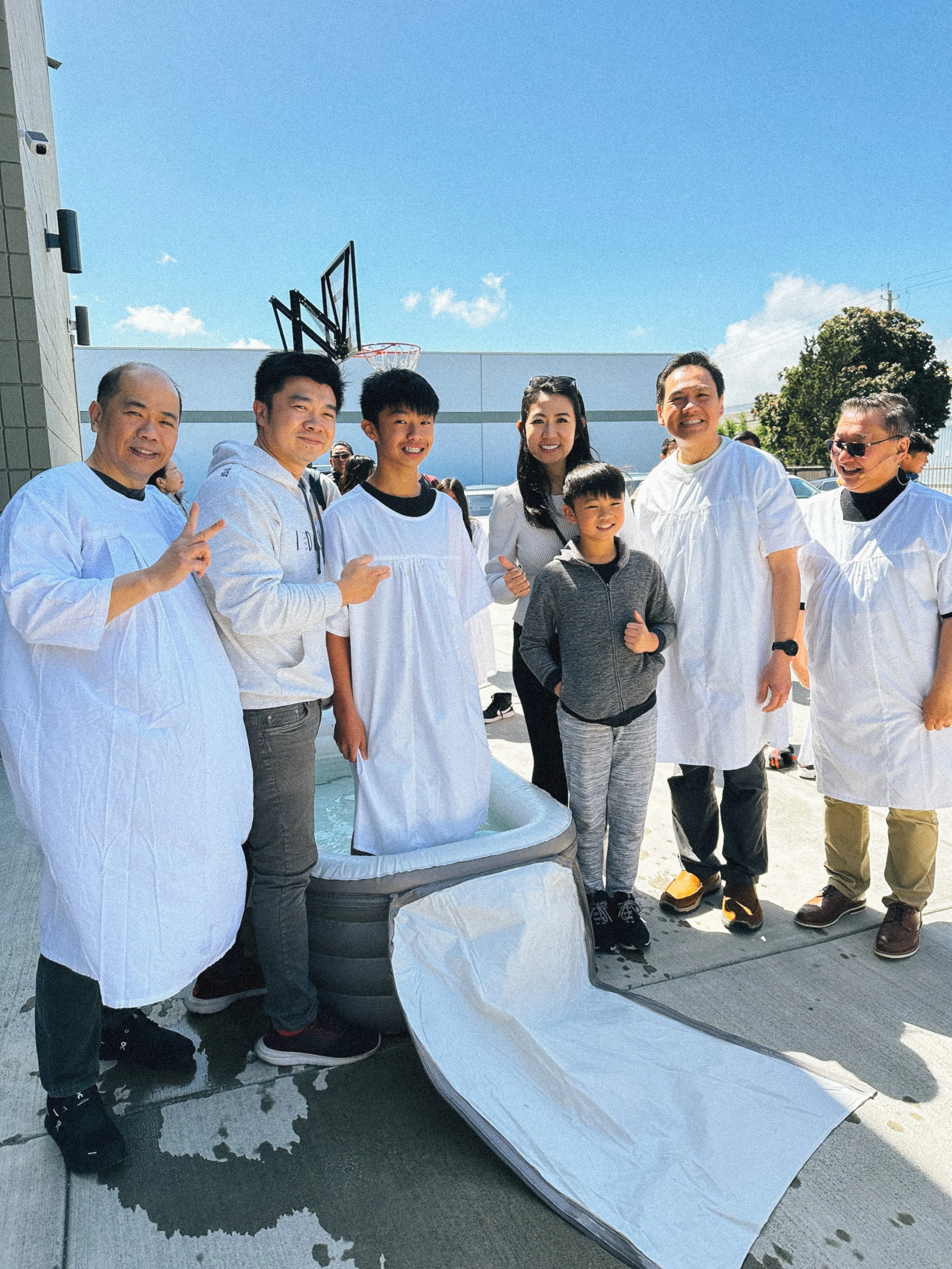 Group of people standing outside on a clear day, posing for a photo commemorating a recent baptism.