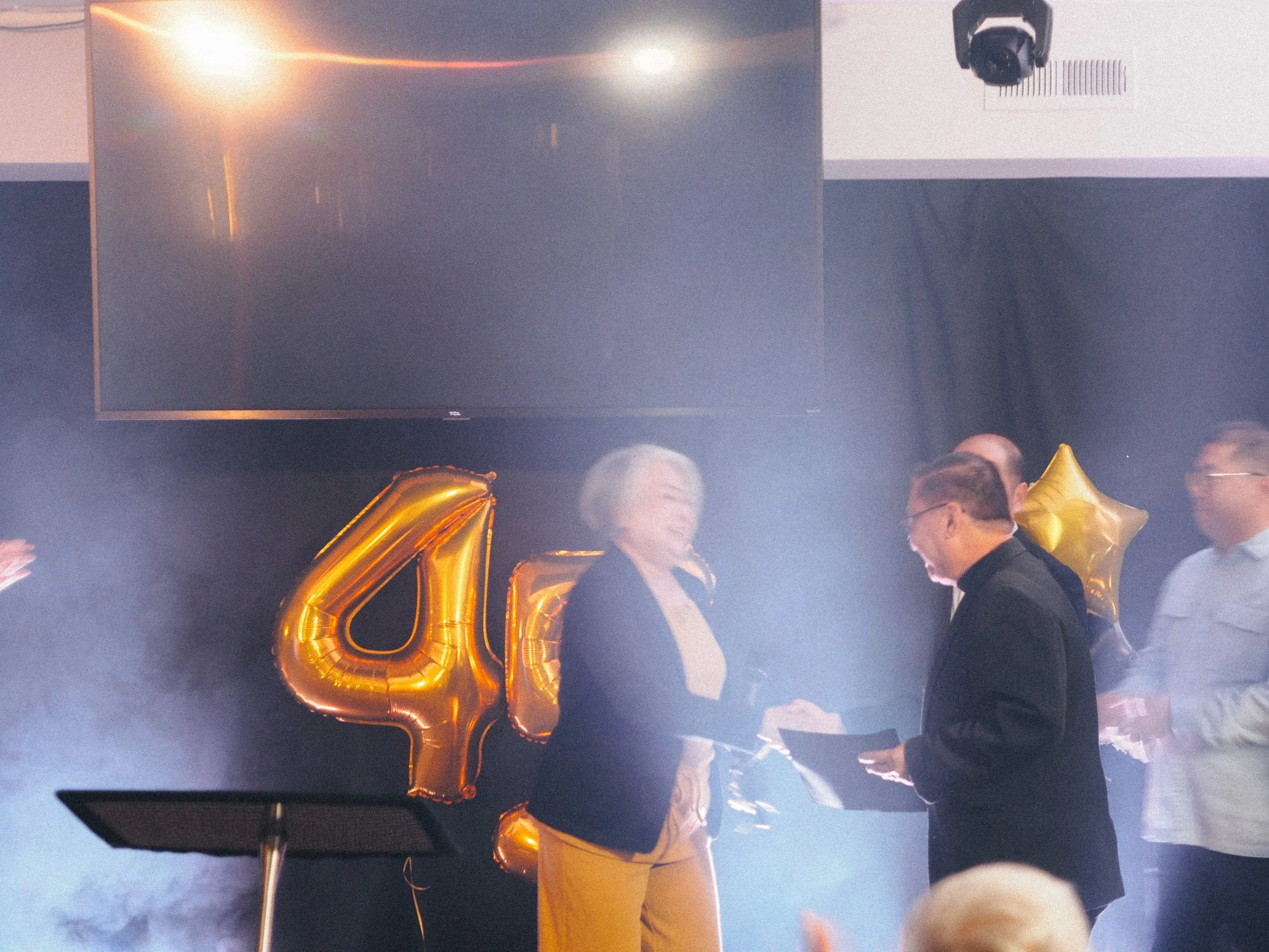 People celebrating an anniversary with golden balloons shaped as the number 45, shrouded in mist or smoke.