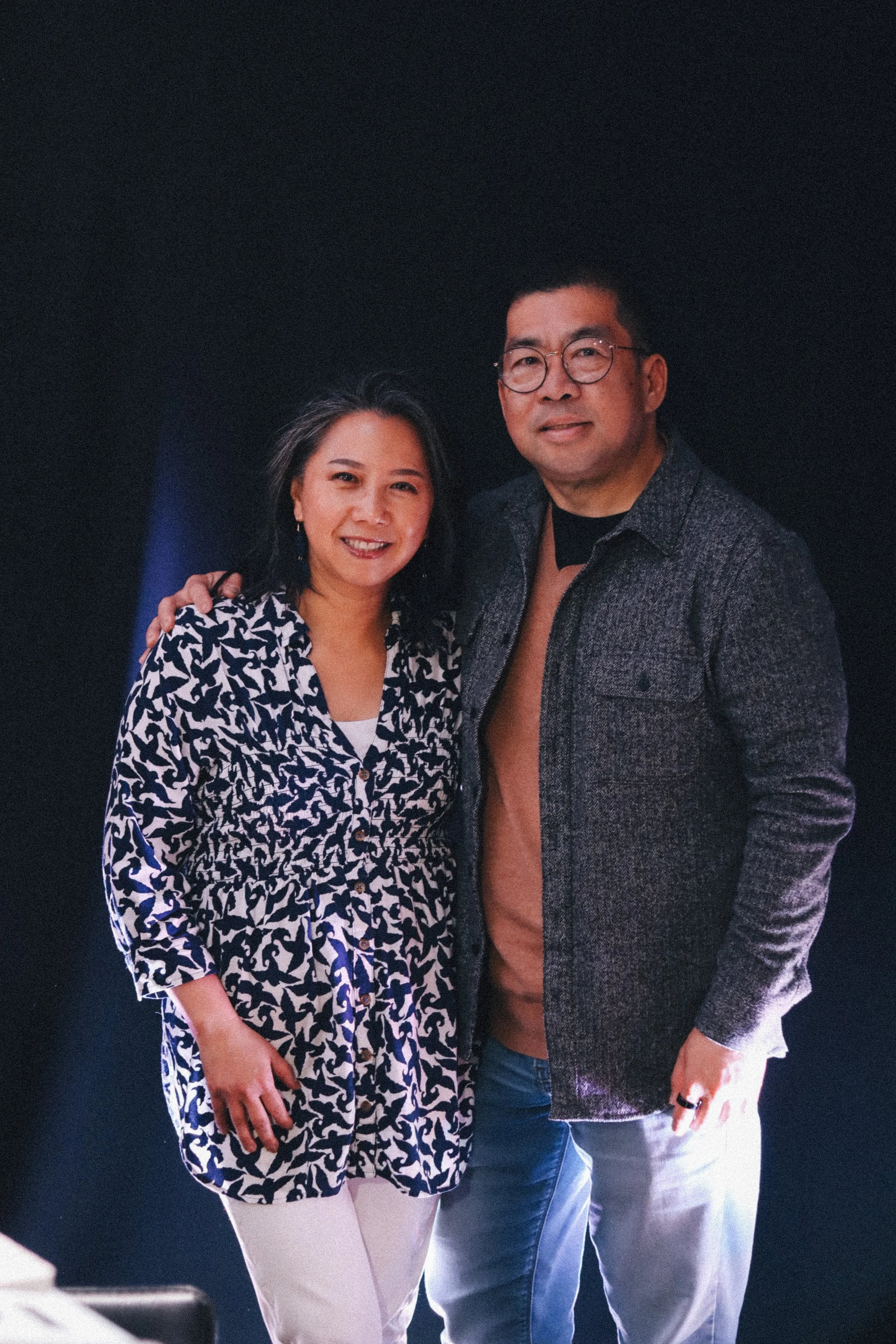 Associate Pastor Hendra and his wife Mercy standing close together, smiling, with a dark background.