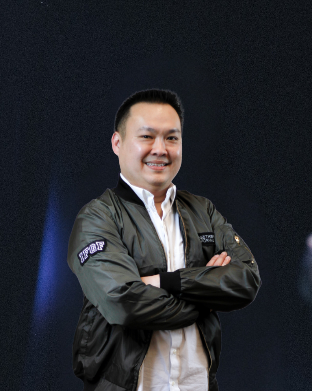 Associate Pastor Yoga with crossed arms, smiling, wearing a black jacket over a white shirt, against a dark background.