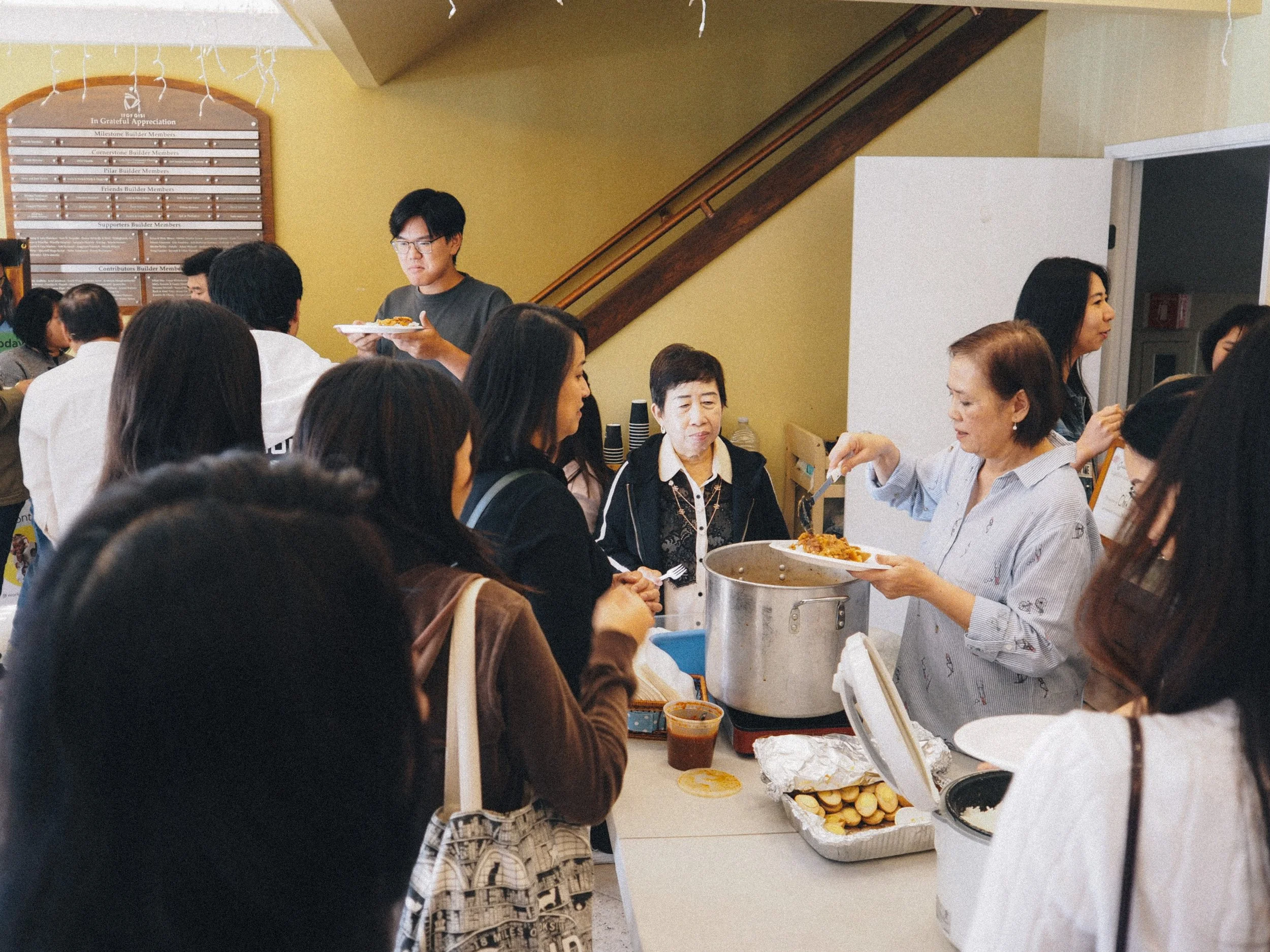 People serving and receiving food at a buffet table in an indoor setting.