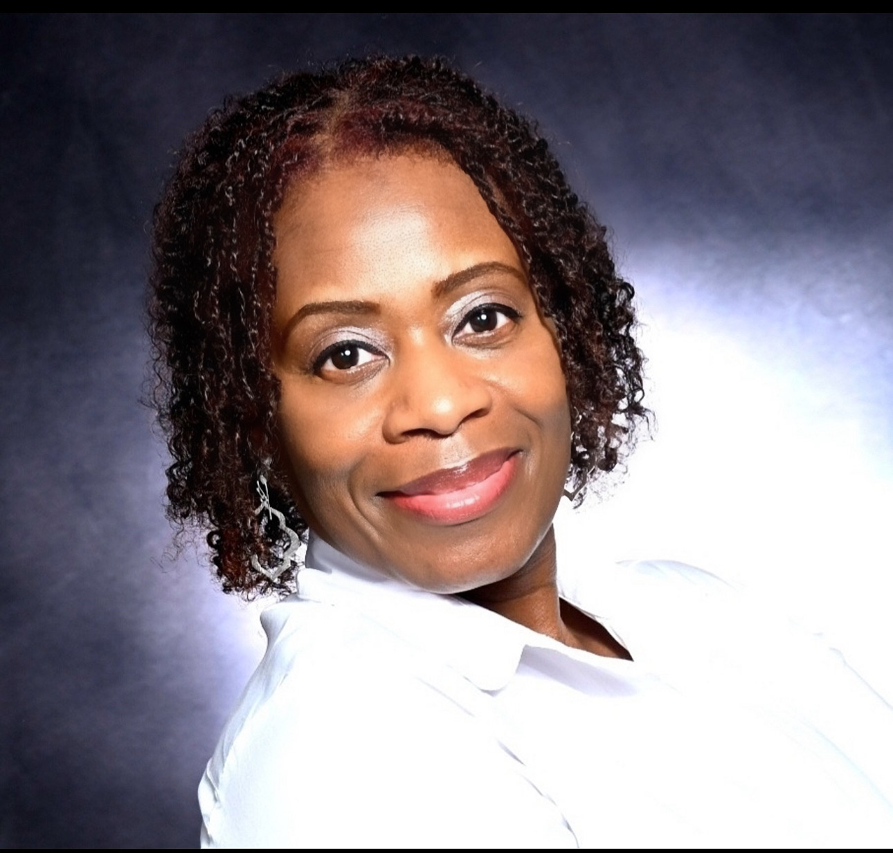 Portrait of a smiling African American woman with short curly hair, wearing a white top against a dark background.