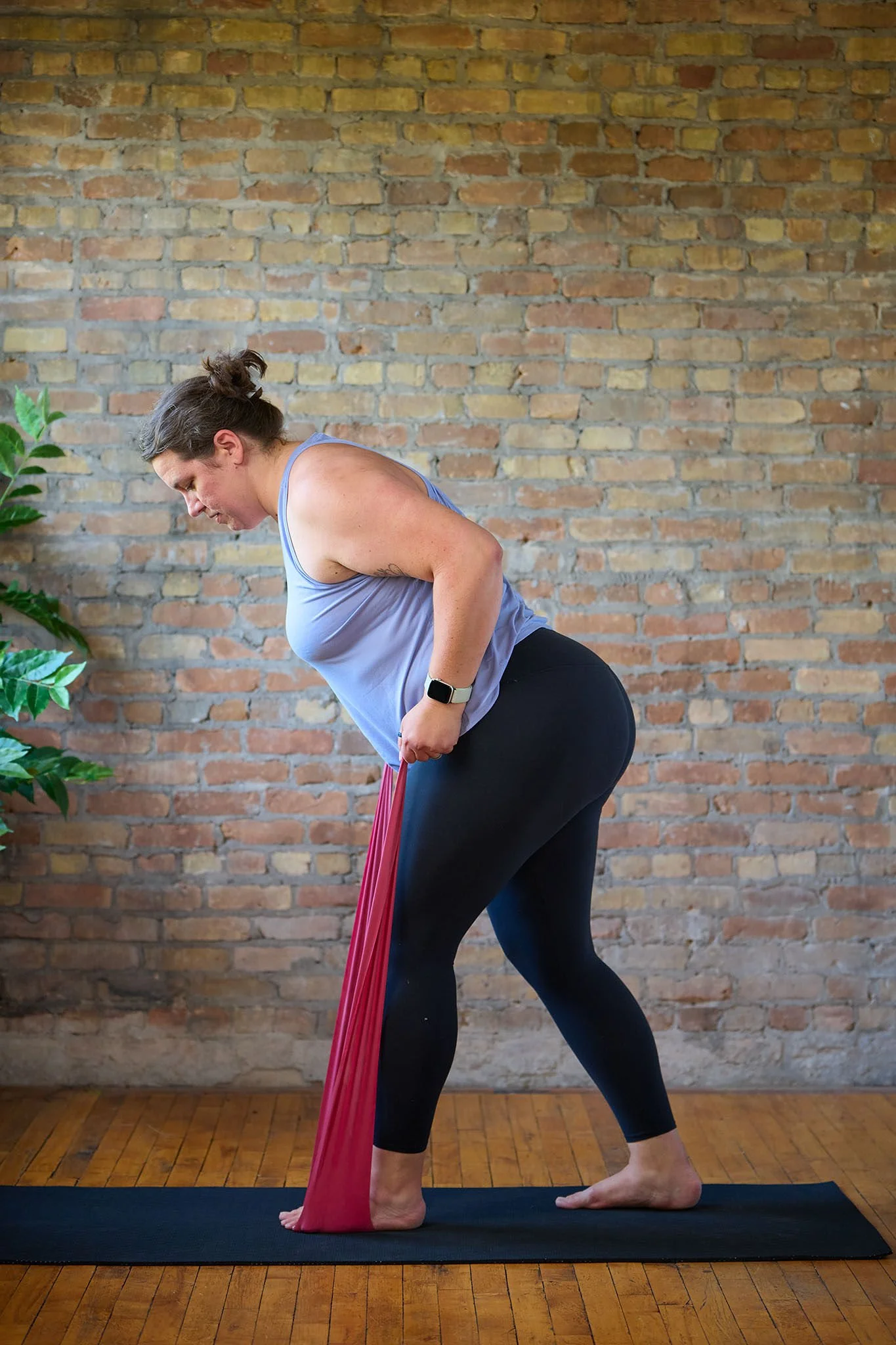 Marta is leaning over while standing, holding a stretch band. She is doing a row exercise.