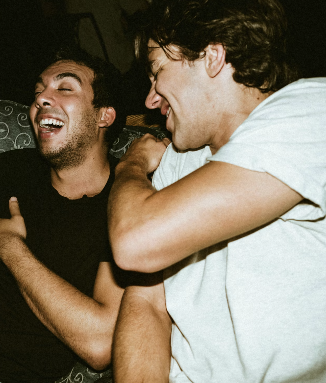 Two men laughing and cuddling on a couch, showing friendship and happiness.