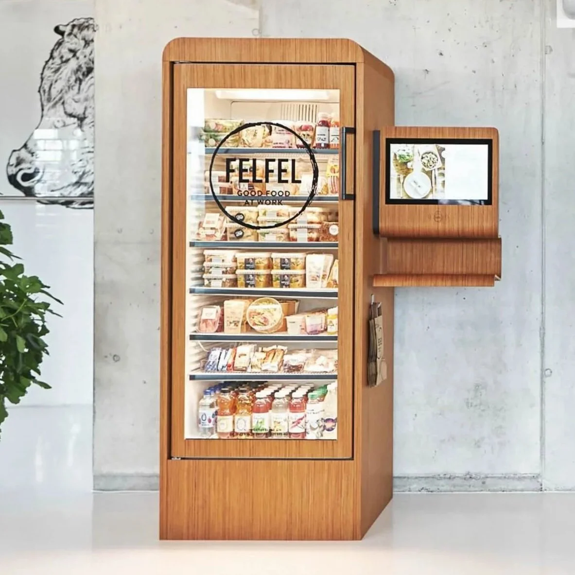 Two women standing in front of a refrigerated vending machine filled with various packaged snacks and beverages in a modern store or café.