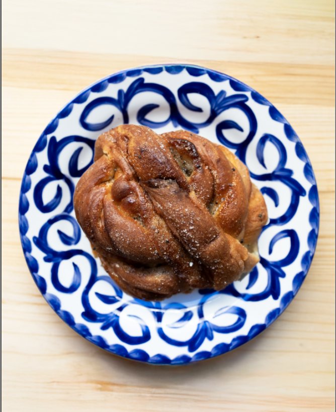 A cinnamon roll dusted with powdered sugar on a blue and white decorative plate, placed on a light wooden surface.