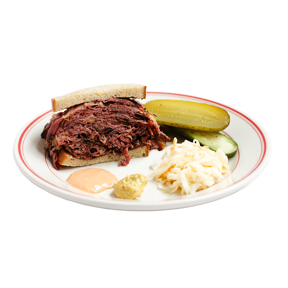 A plate of the classic New York-style pastrami sandwich with pickles, mustard, and coleslaw.
