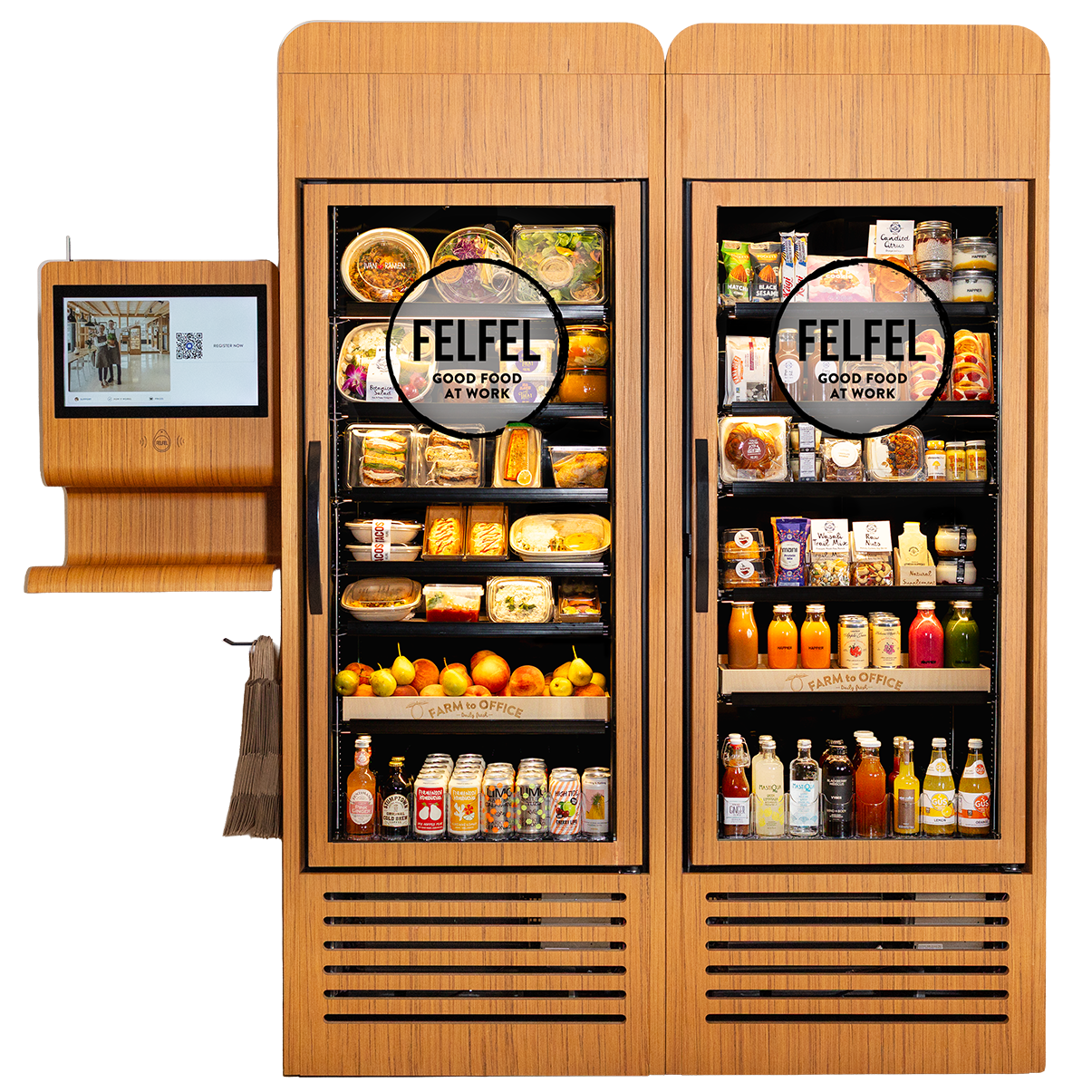A wooden vending machine with two sections filled with food and beverages, labeled 'FELFEL GOOD FOOD AT WORK,' a screen on the left displays a person in a store, and a small table with a paper bag and canvas bag is beneath the screen.