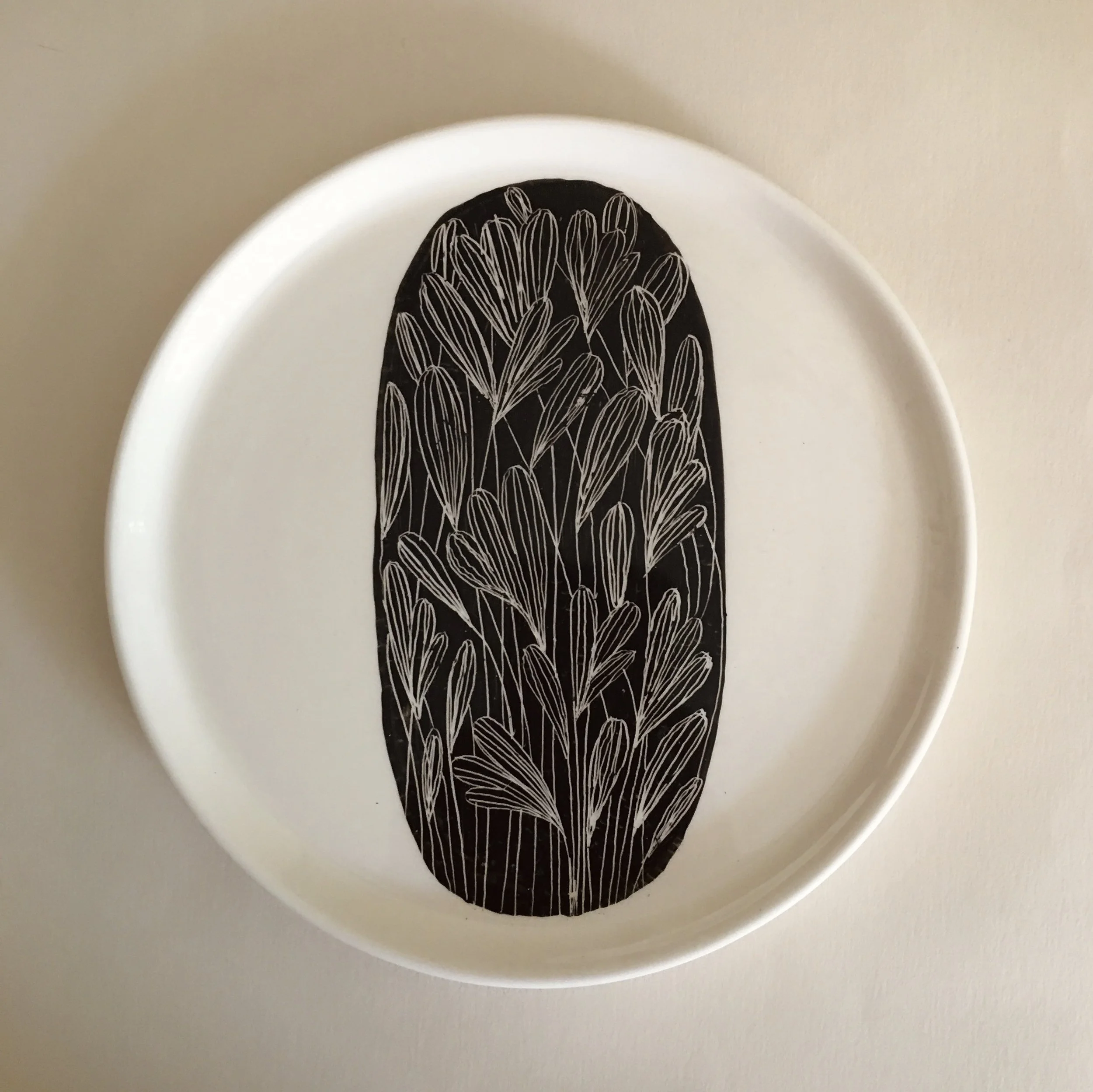 Decorative plate with black oval design featuring white outlined leaves.