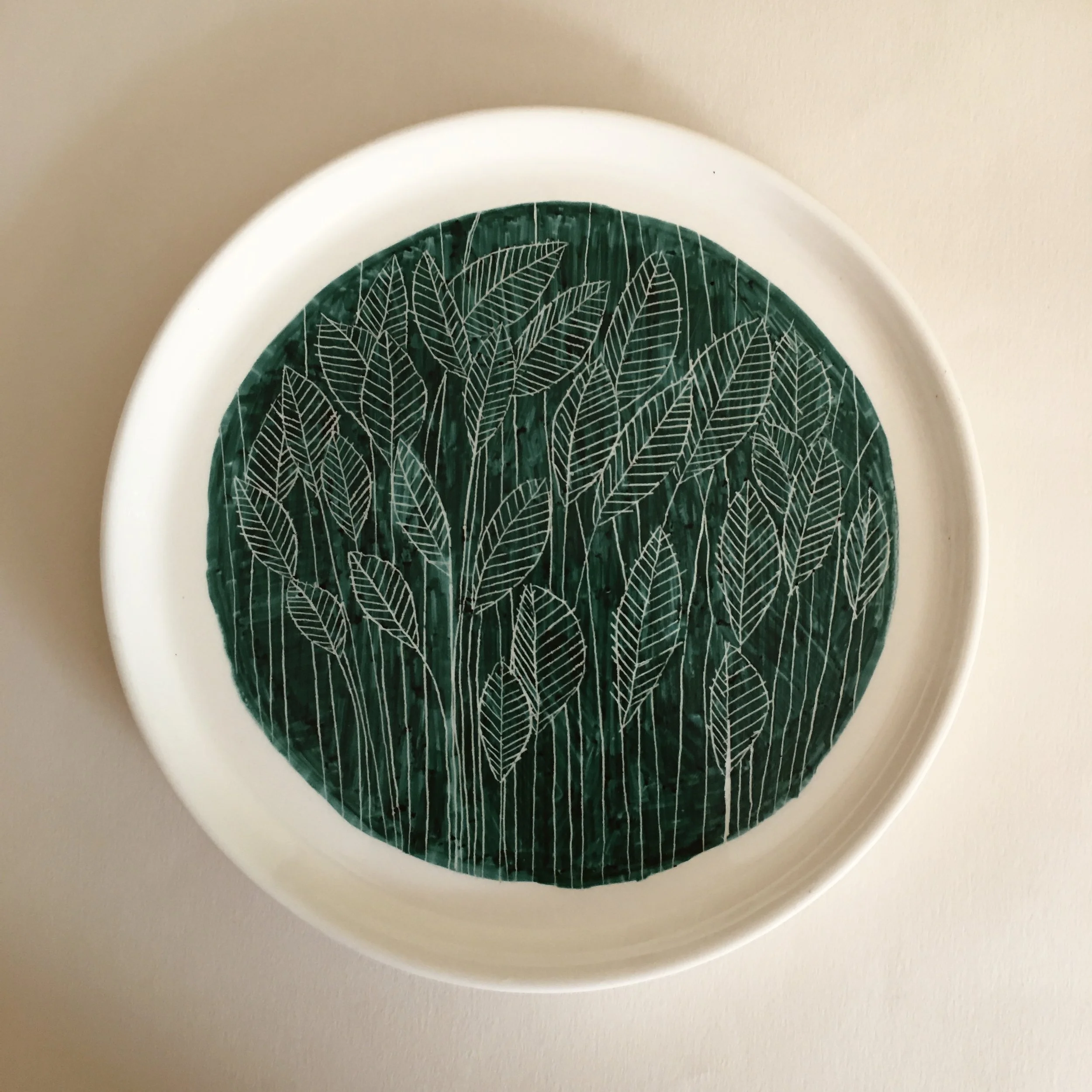 Decorative plate with a green background and white leaf pattern.