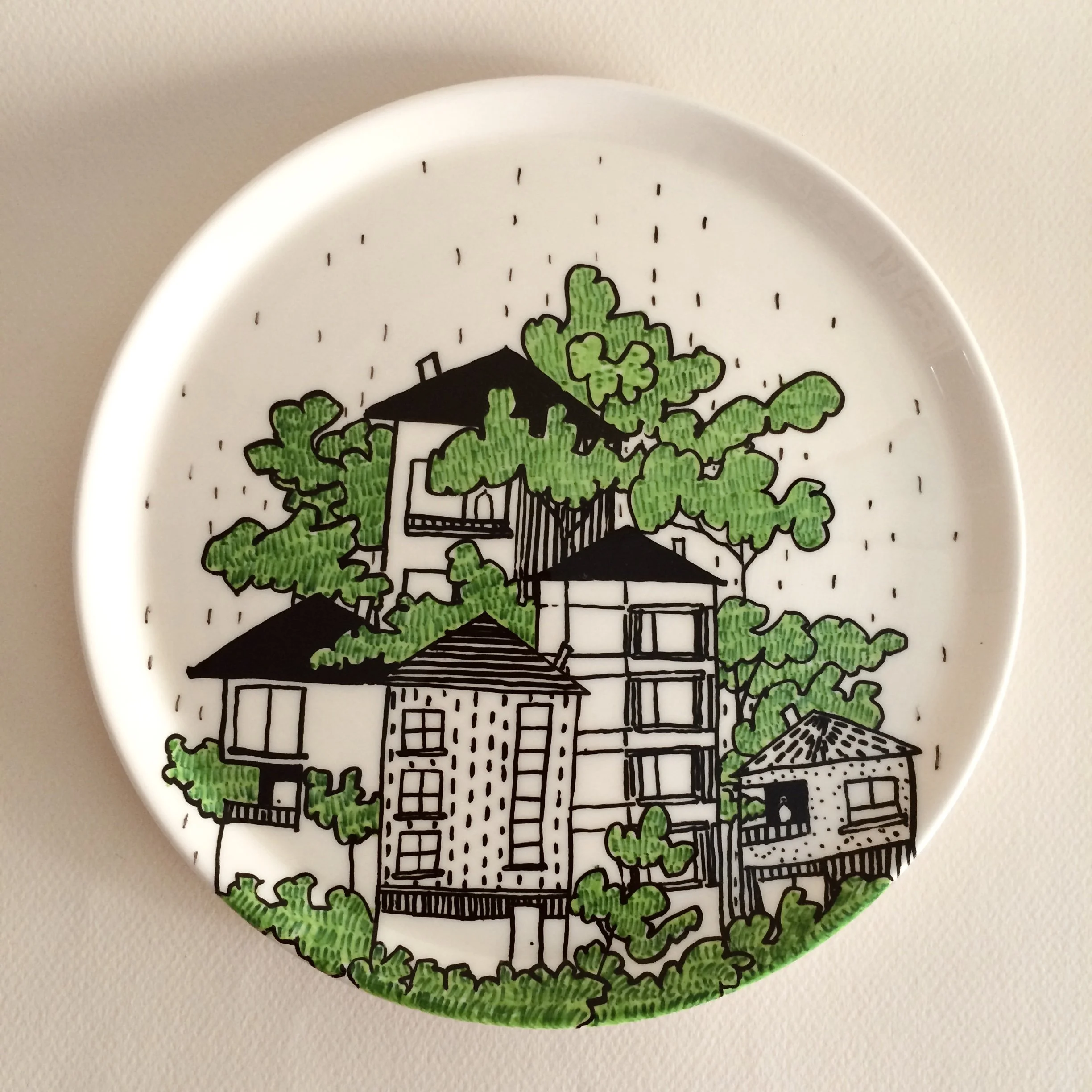Decorative ceramic plate featuring black and white illustrations of houses and green trees.