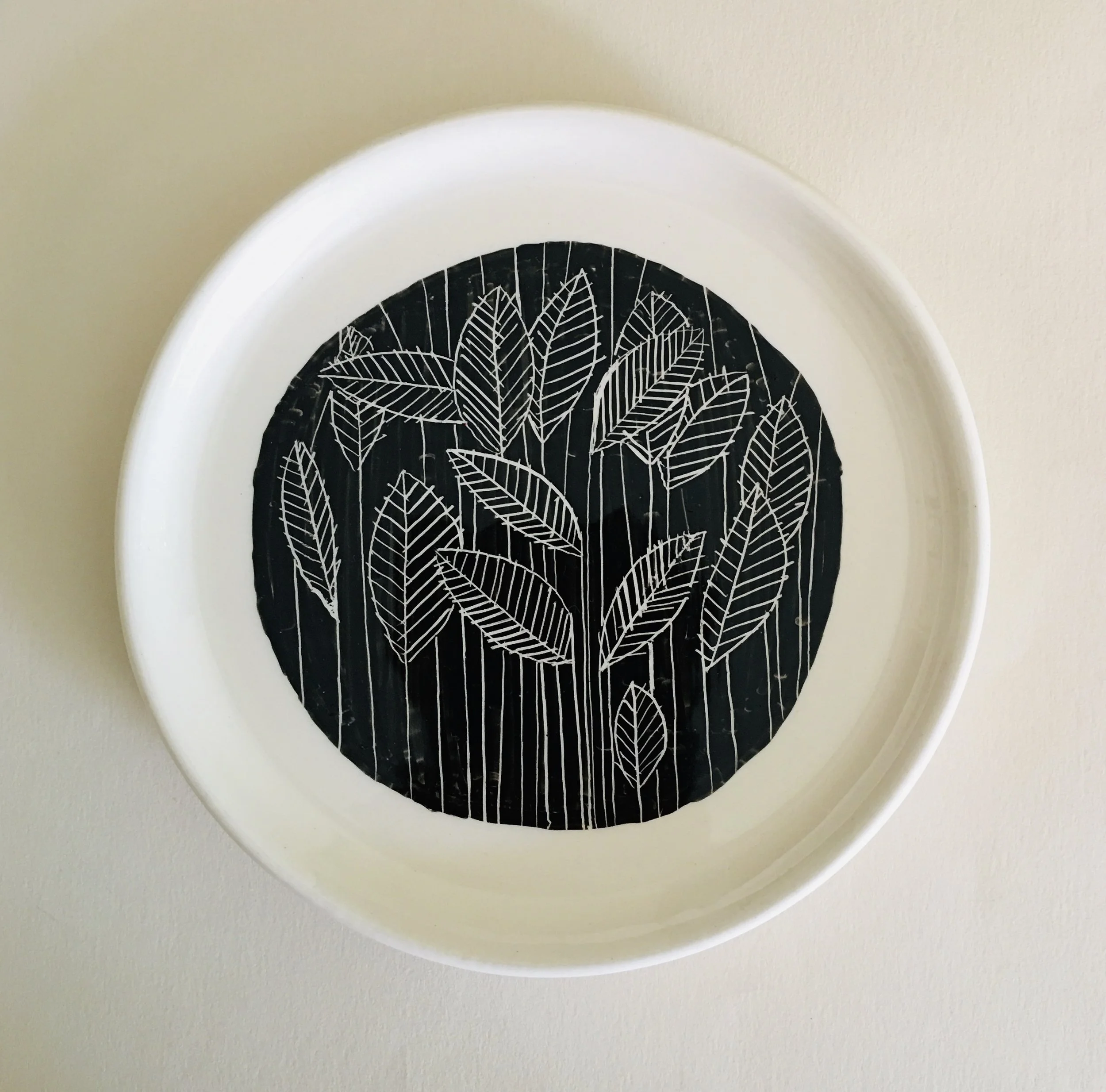 White round tray with black interior featuring white line drawing of leaves.