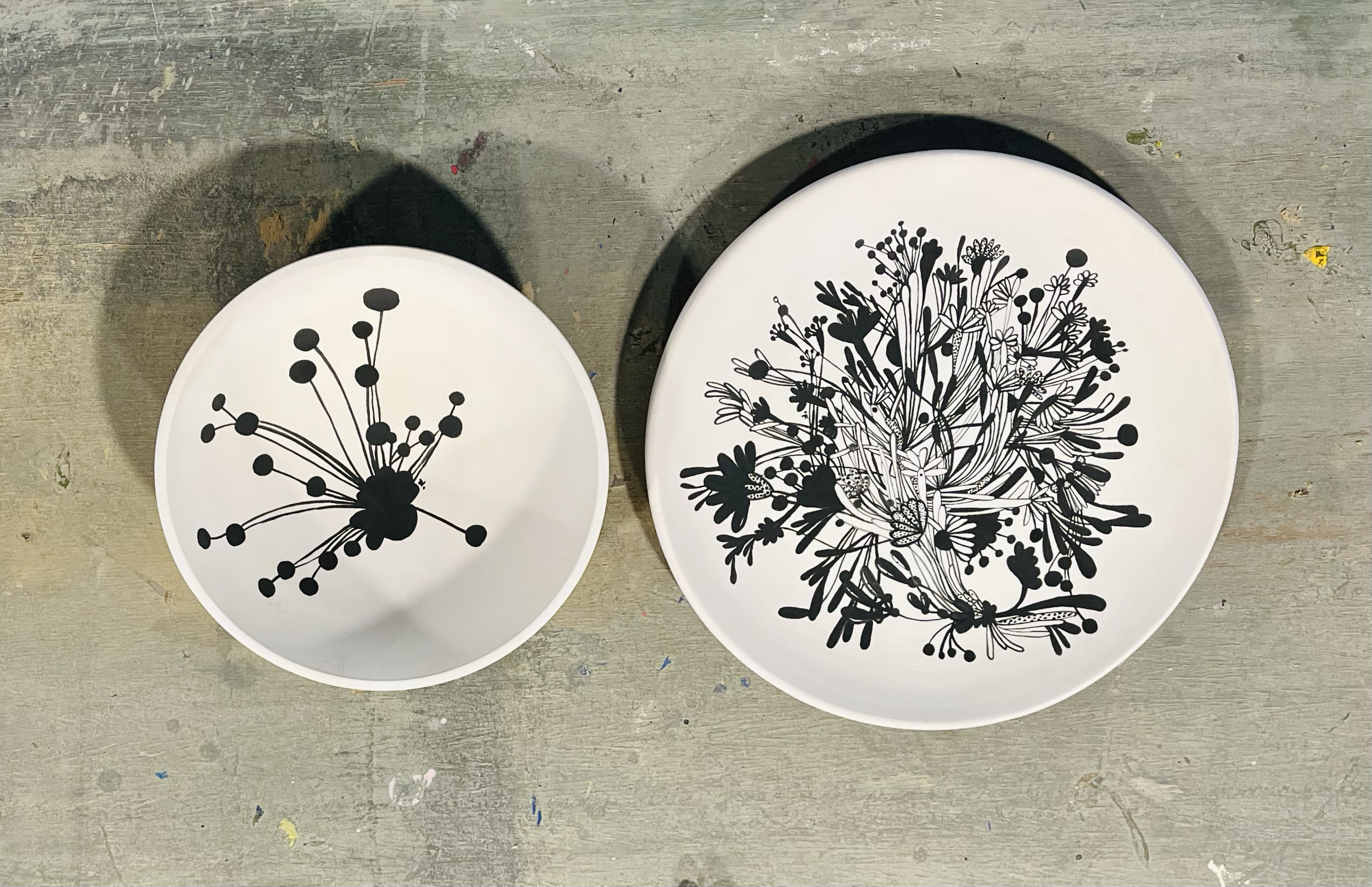 Two white plates with black floral and botanical designs on a wooden surface.