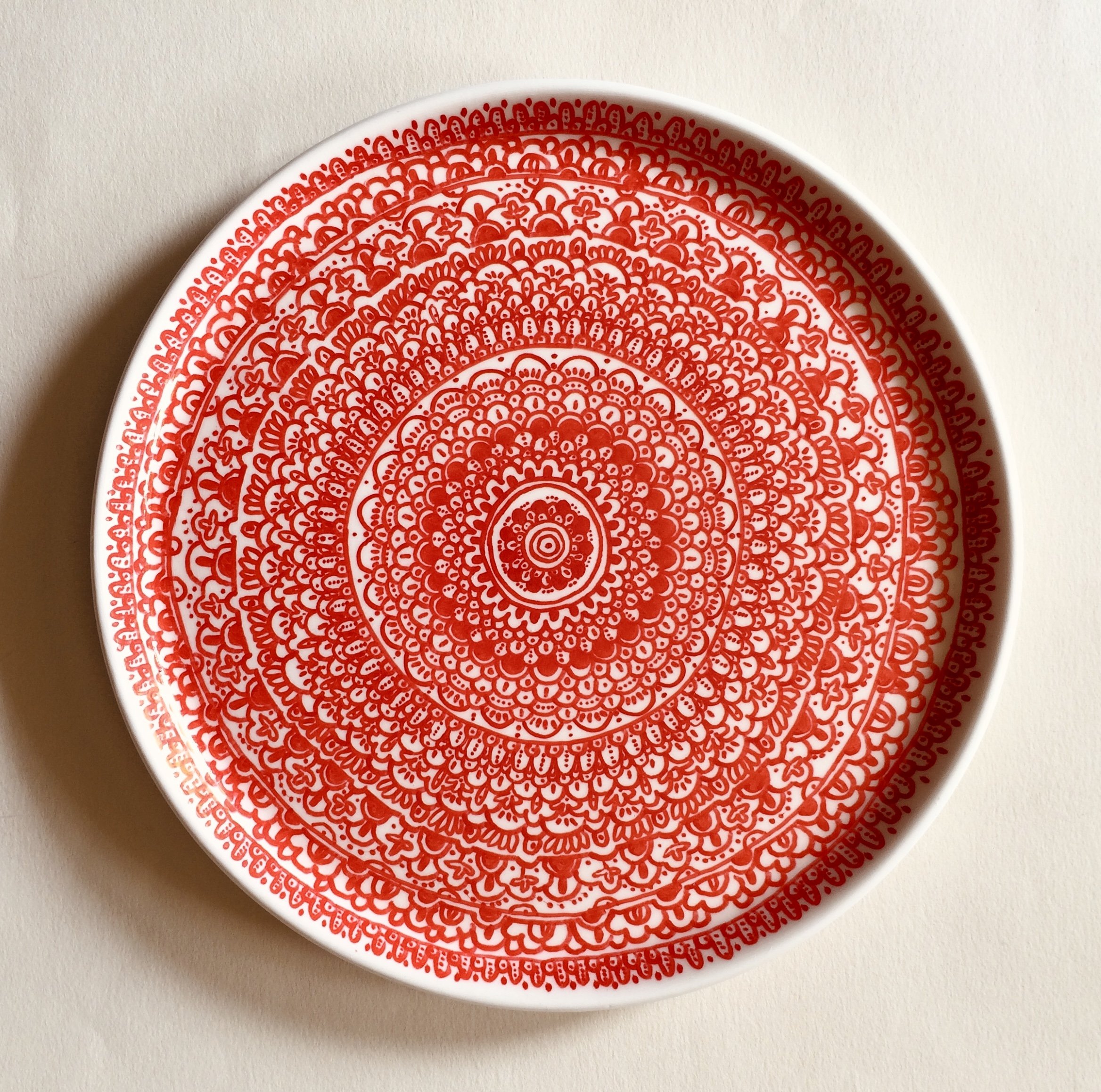 Round decorative plate with intricate red mandala pattern on a white background.