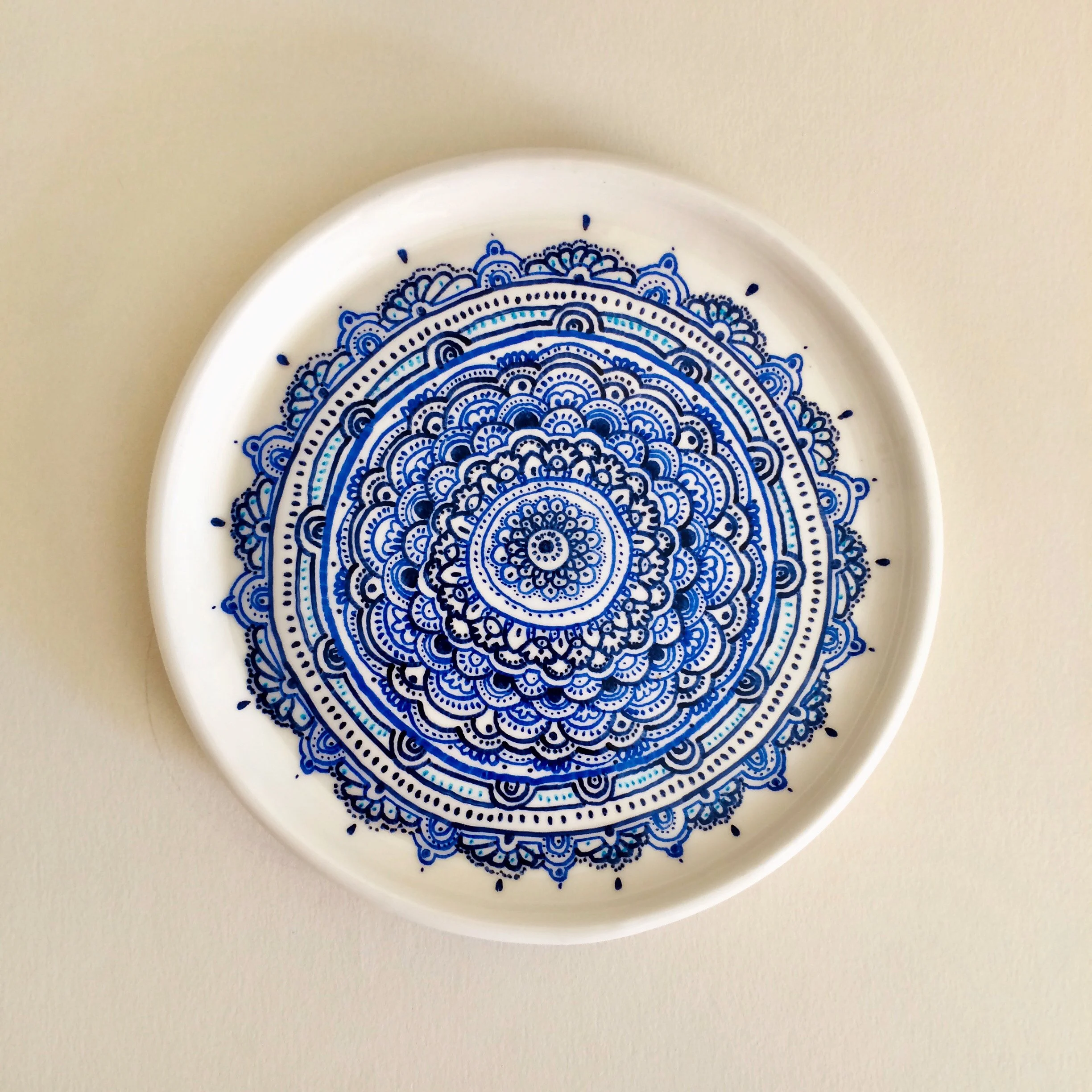 White round plate with intricate blue mandala design on a white surface.