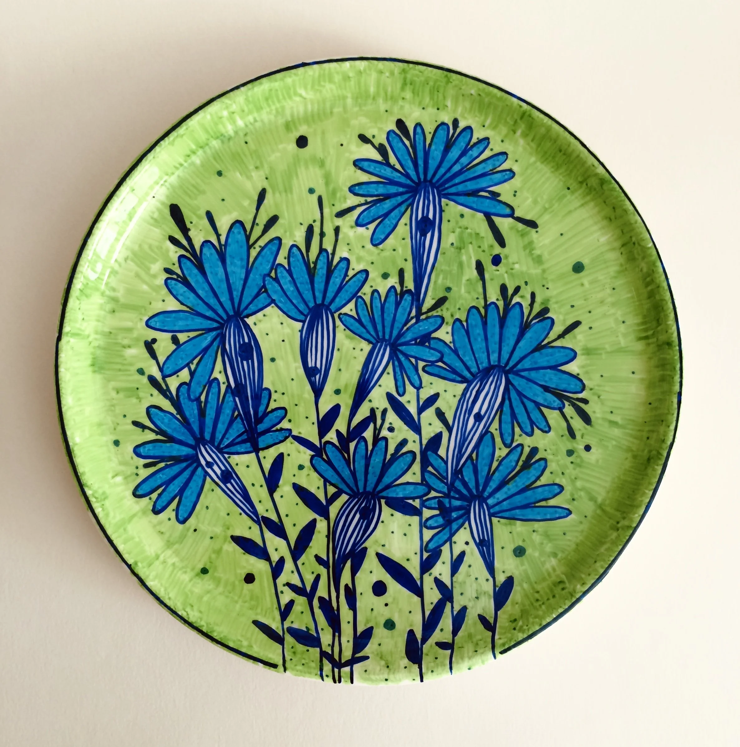 Decorative round plate with a green background and blue floral design featuring daisies.