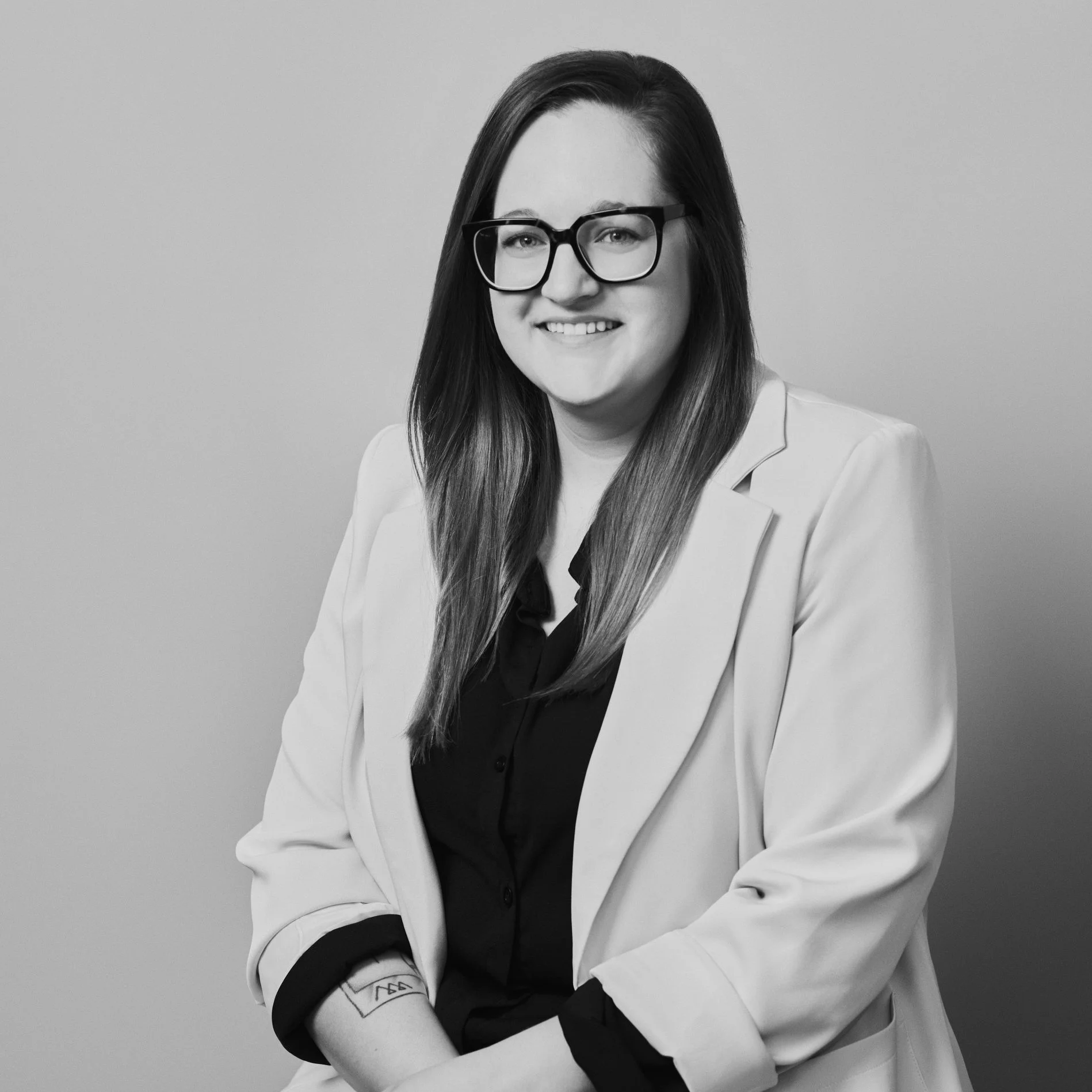 Portrait en noir et blanc d'une femme souriante portant des lunettes et une veste claire.
