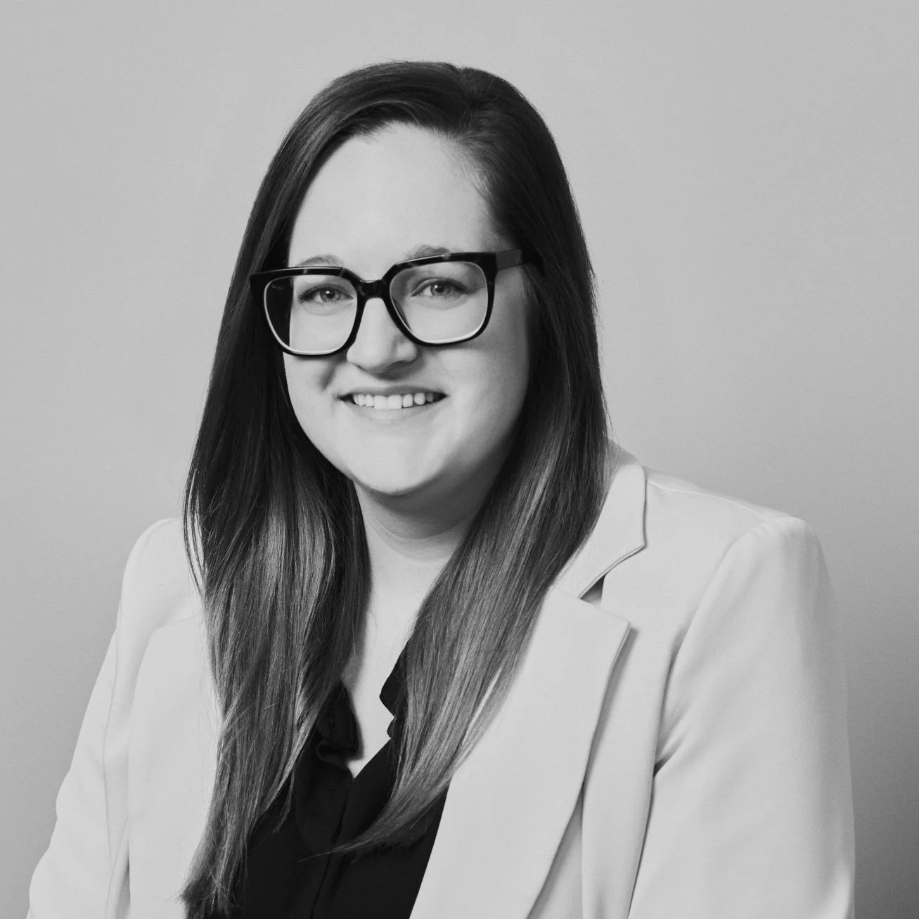 Portrait en noir et blanc d'une femme souriante portant des lunettes et une veste claire.